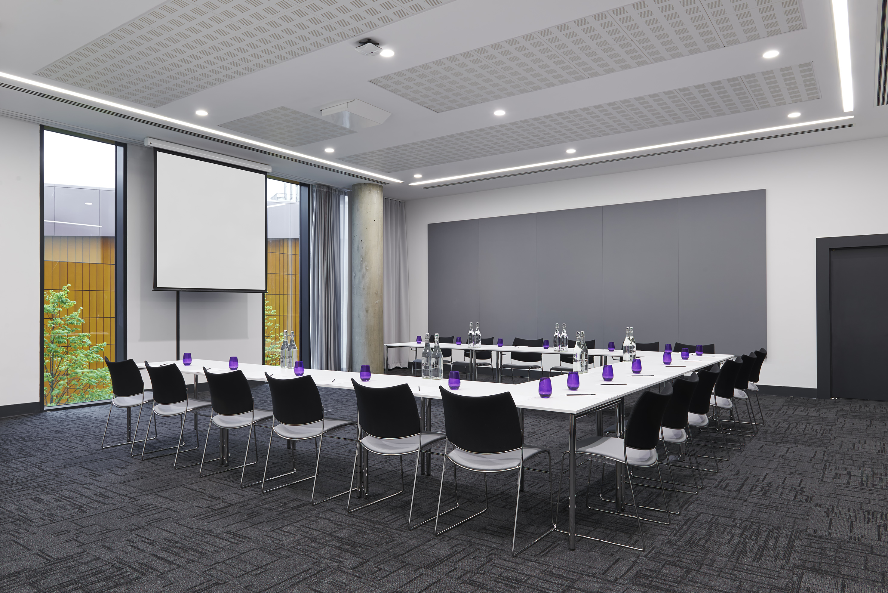 Modern conference room with U-shaped table, chairs, projector, and natural light.