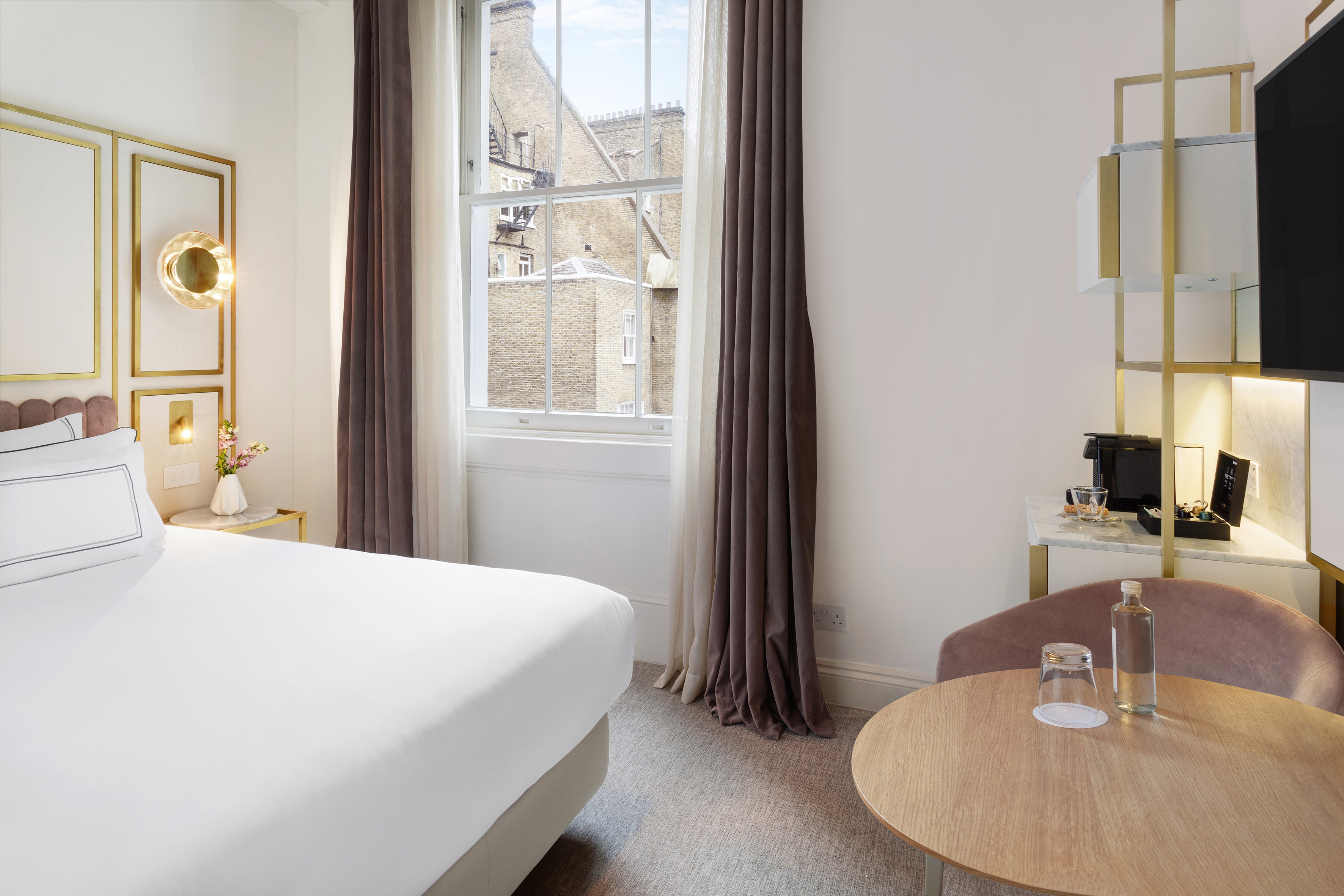 Modern hotel bedroom with bed, gold decor, window city view, coffee station.