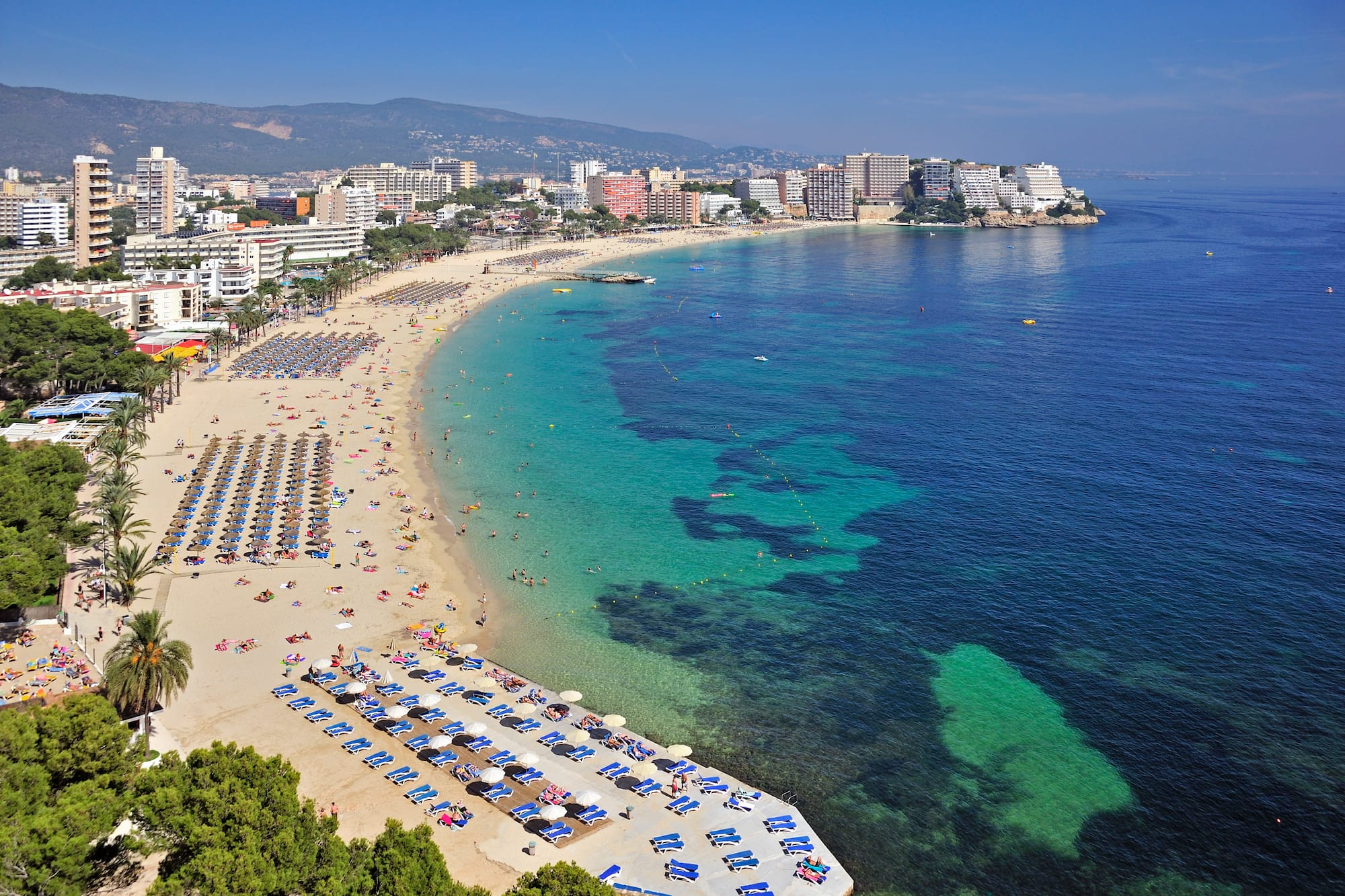 a beach with umbrellas and chairs and buildings in the background