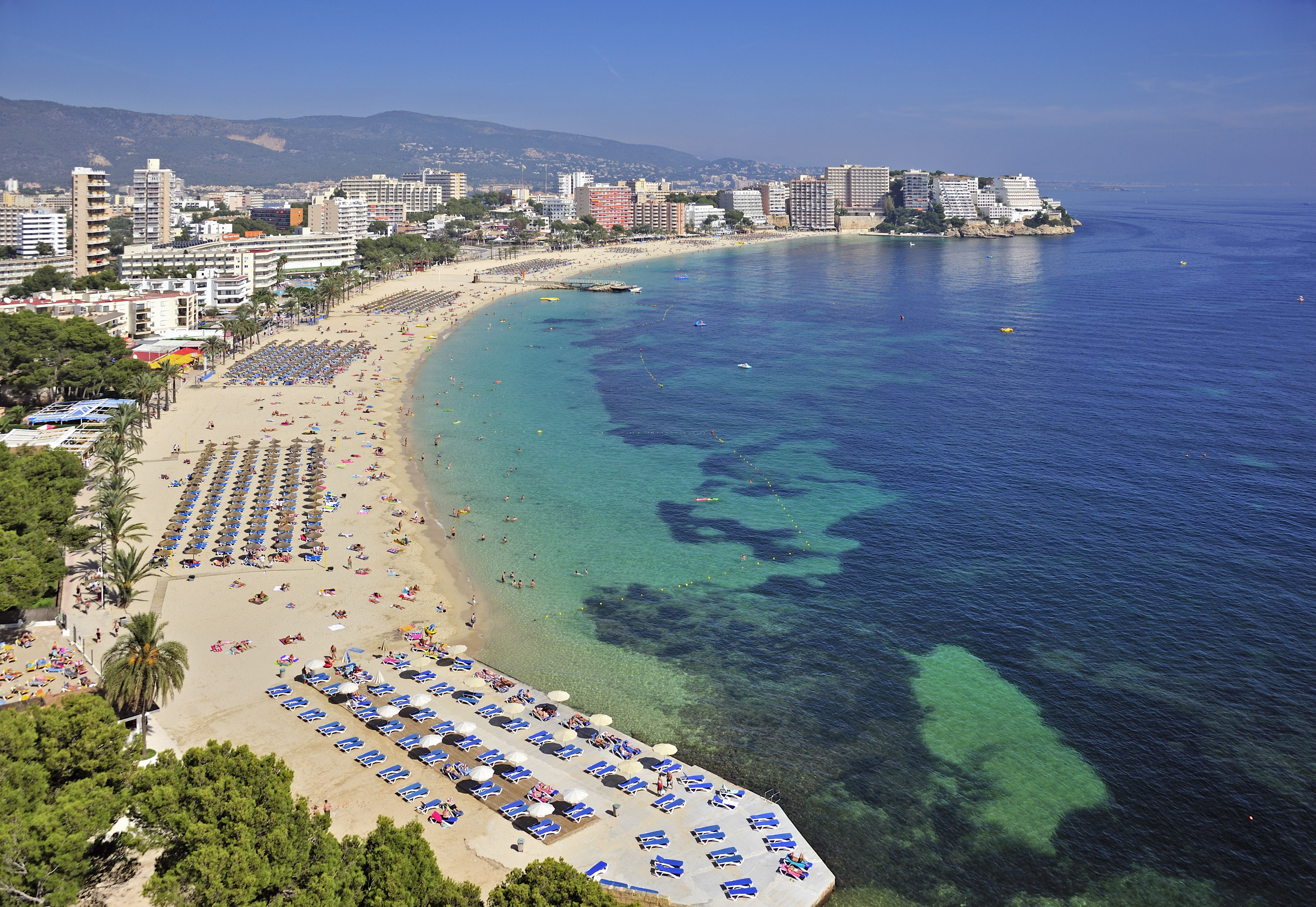a beach with umbrellas and chairs and buildings in the background