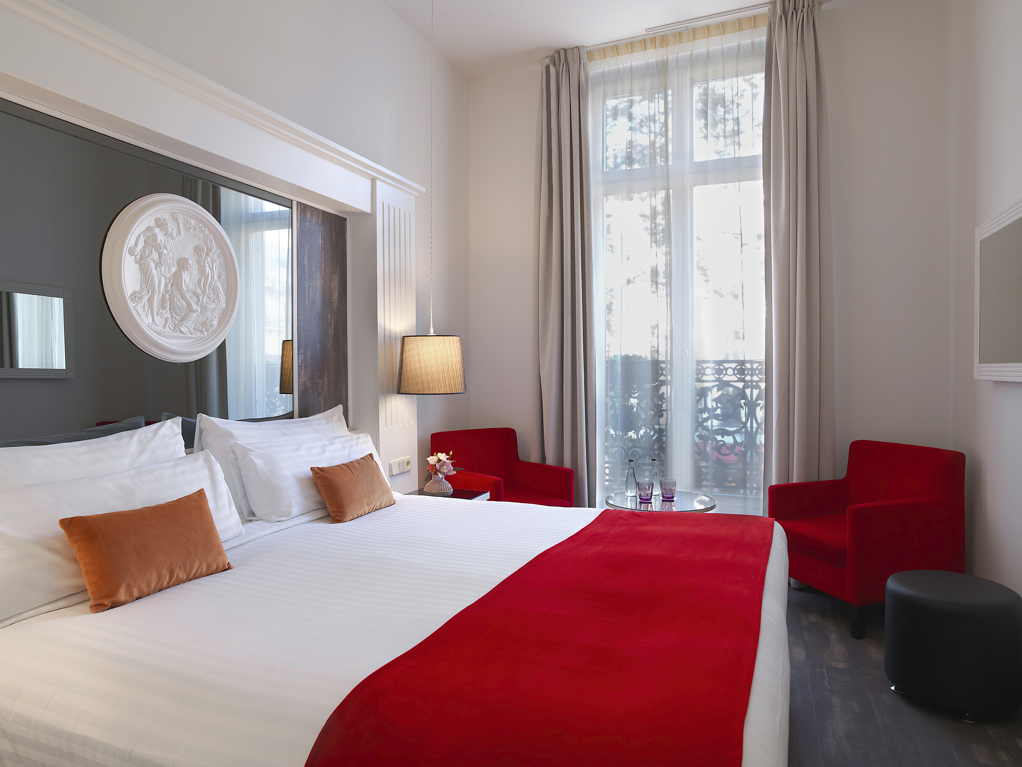Luxury Parisian hotel room with white bed, red accents, and large window.
