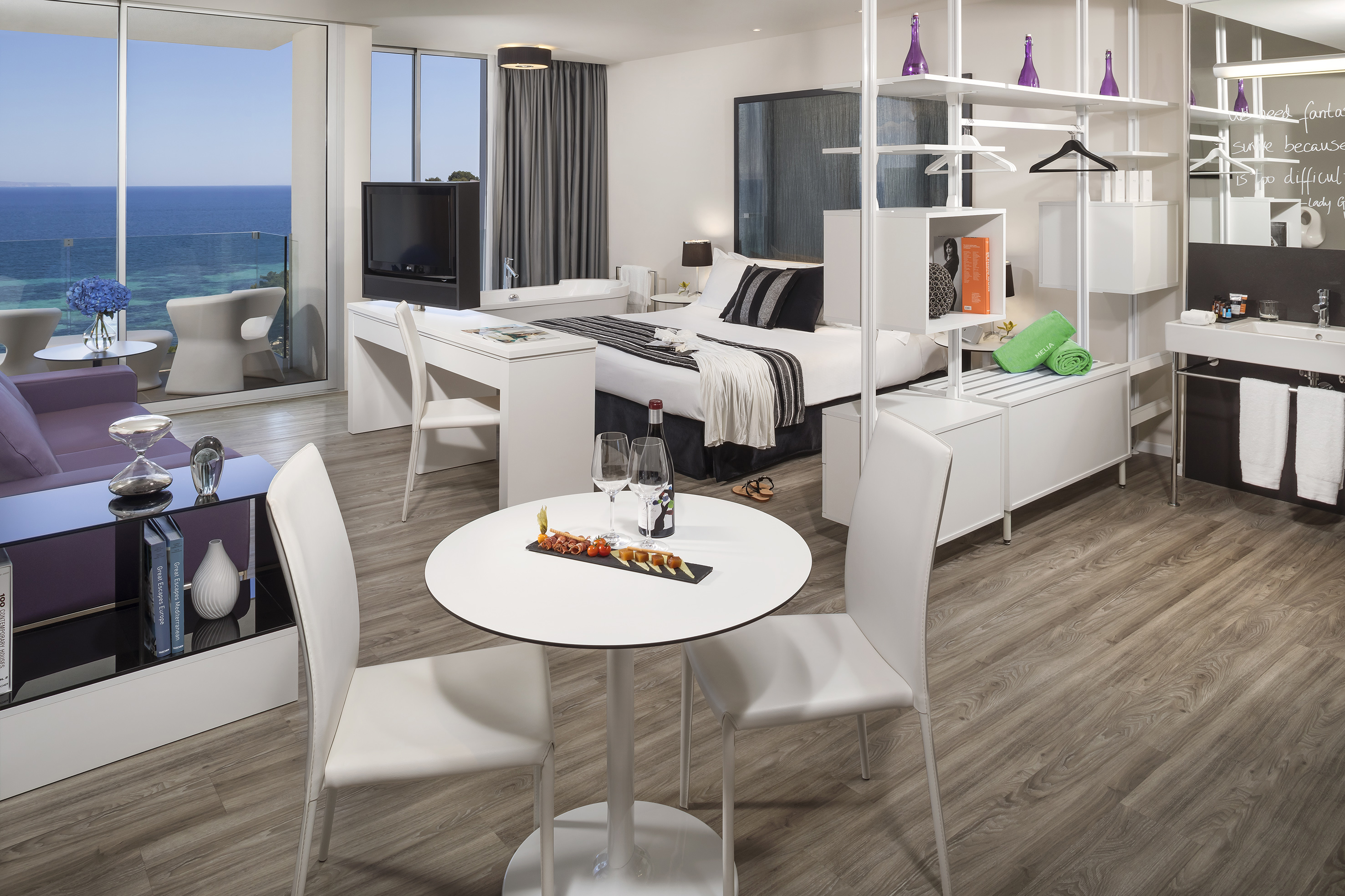 Luxury ocean view hotel suite with modern bed, dining area, and balcony.