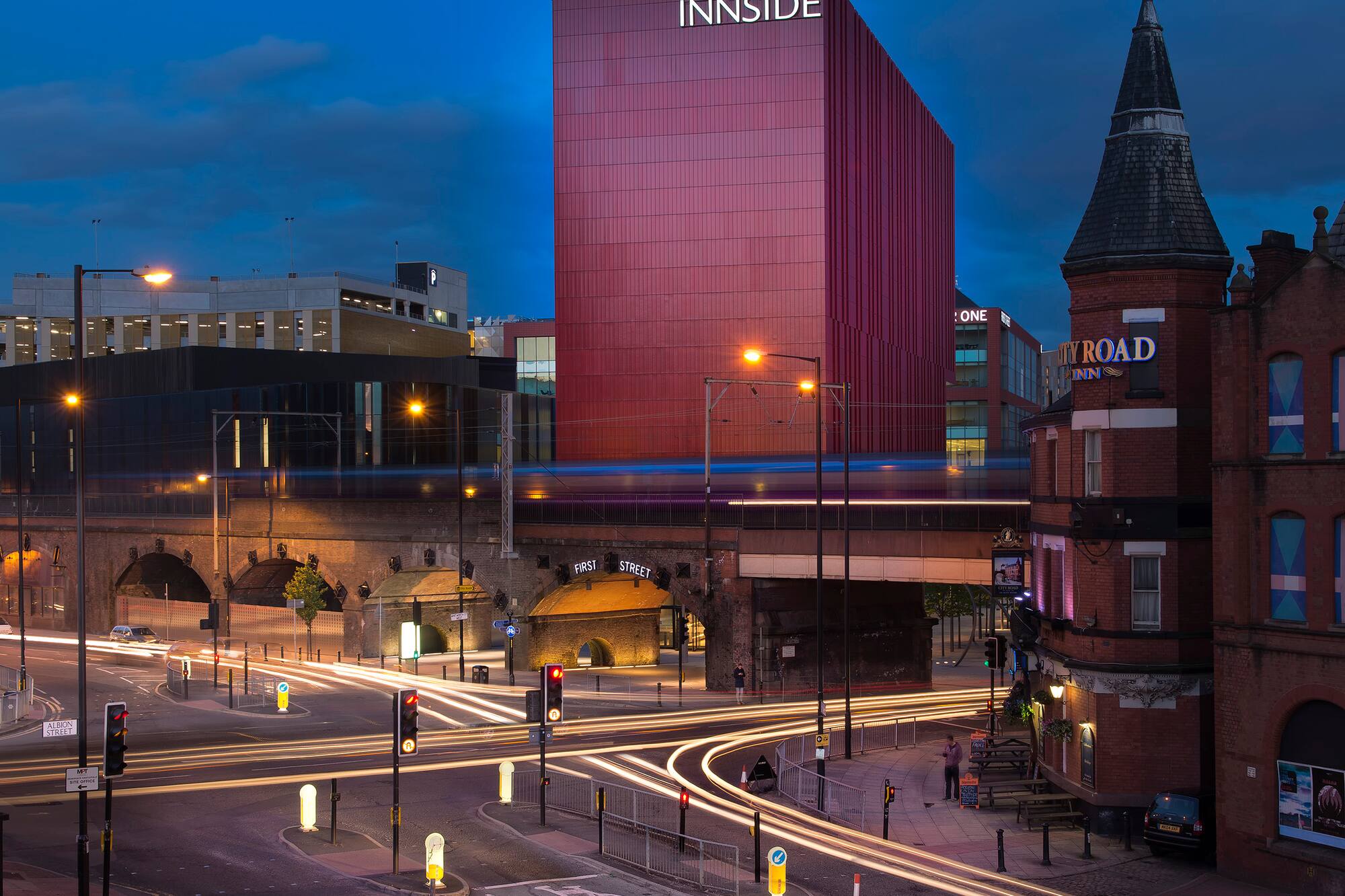 INNSIDE Manchester hotel at dusk, city street with vehicle light trails.