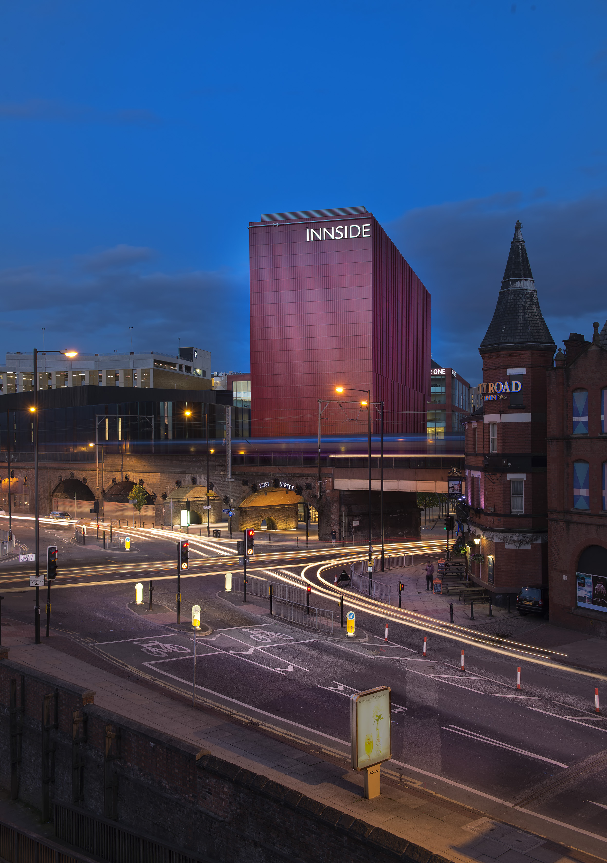 INNSIDE Manchester hotel at dusk, city street with vehicle light trails.