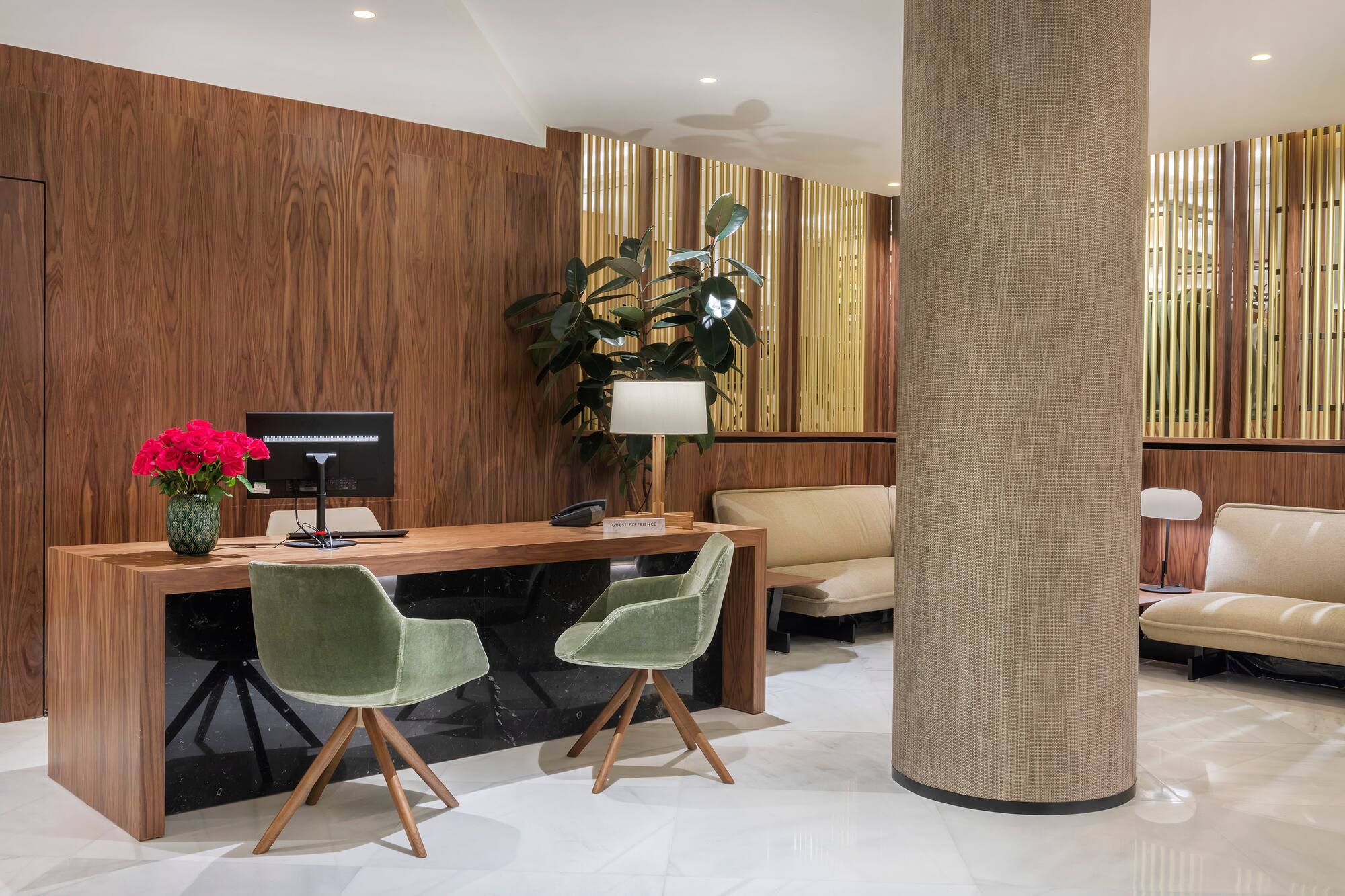 Modern hotel reception desk with green velvet chairs and lounge seating.