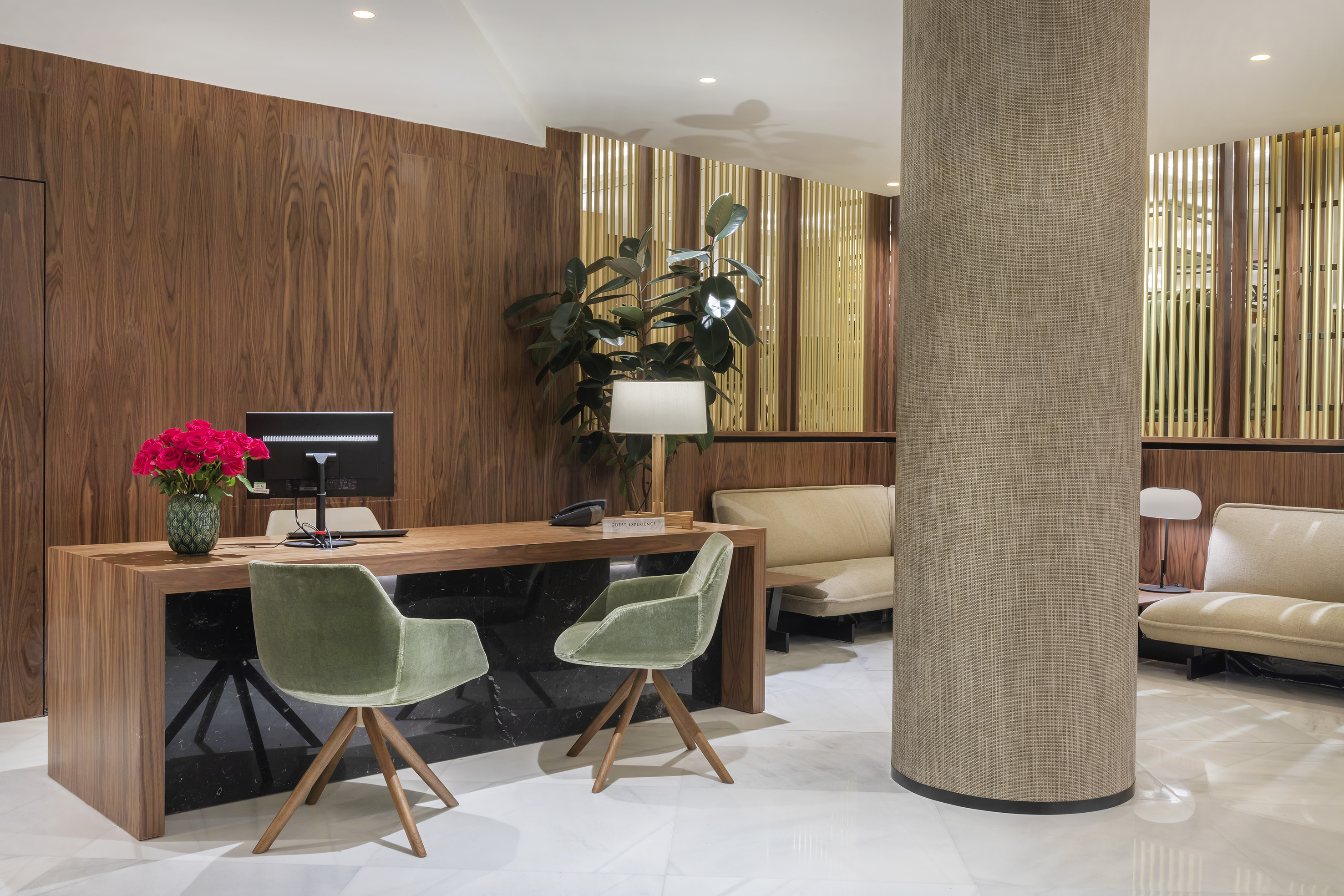 Modern hotel reception desk with green velvet chairs and lounge seating.