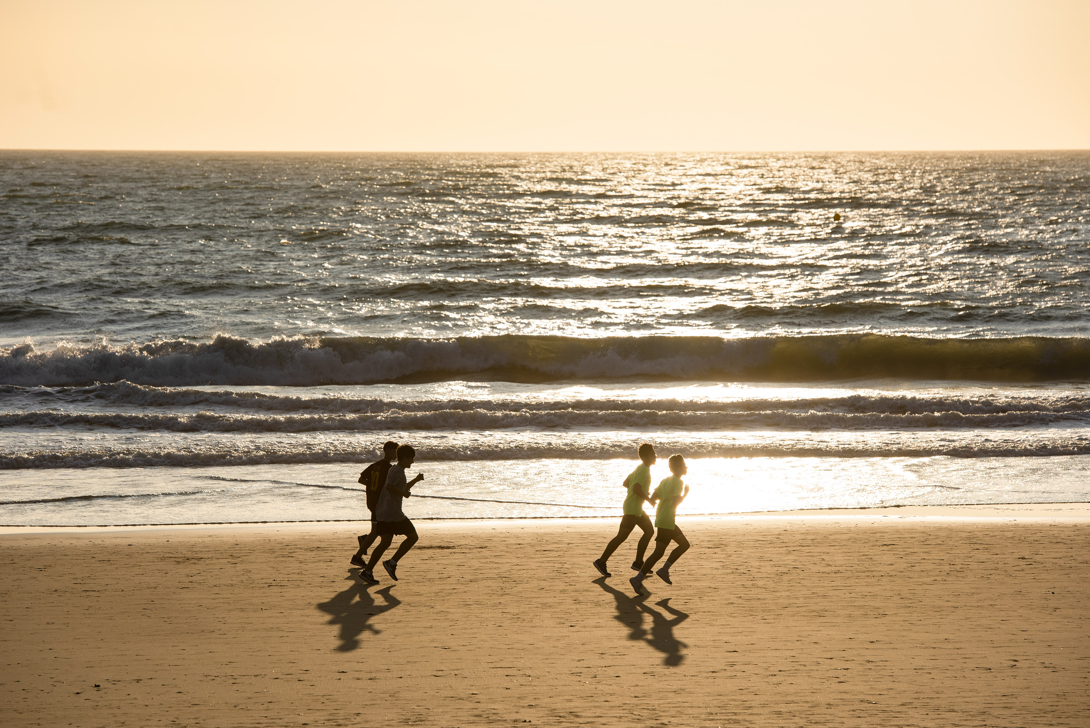 Silhouetted runners exercising on a sandy beach during golden hour sunset.