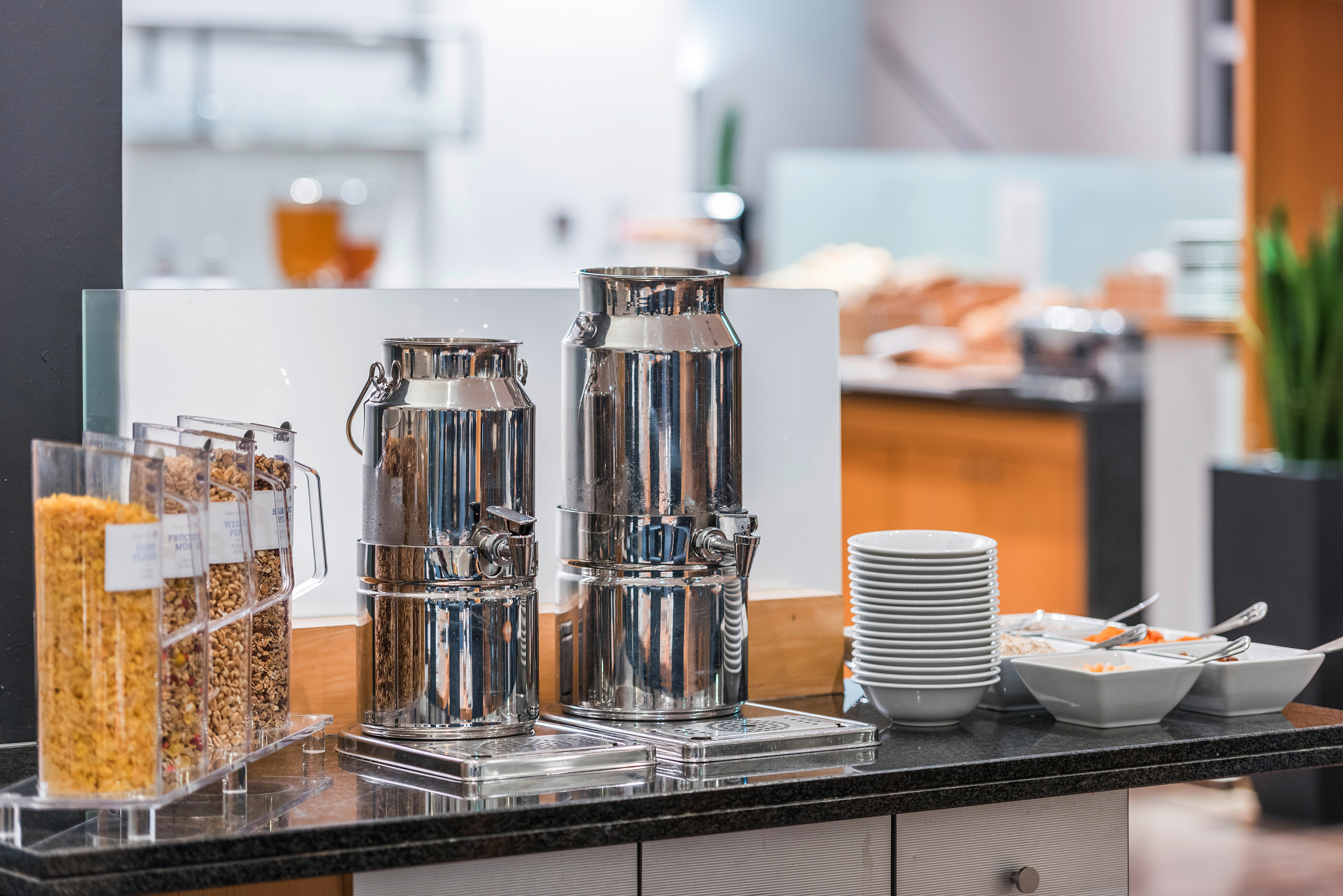 Breakfast buffet with cereal dispensers, milk urns, and white bowls.