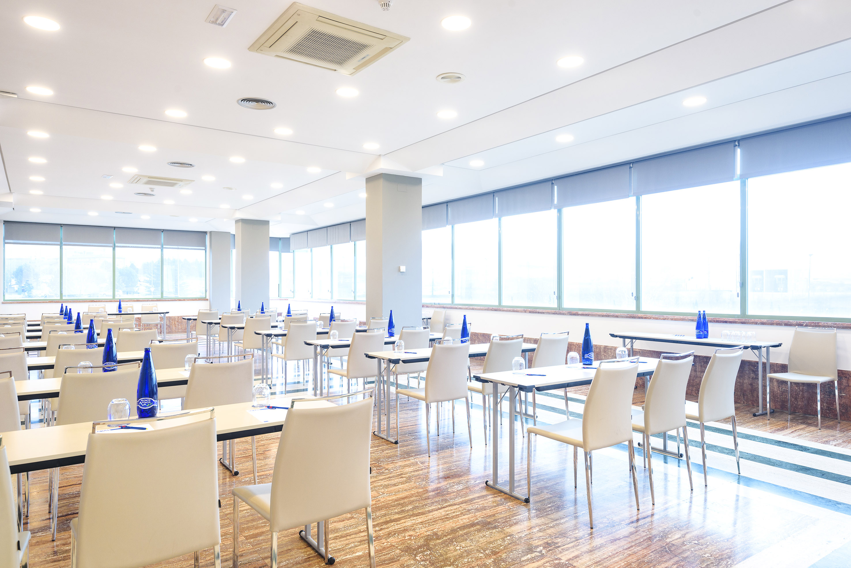 Spacious meeting room with tables, chairs, water bottles, large windows.