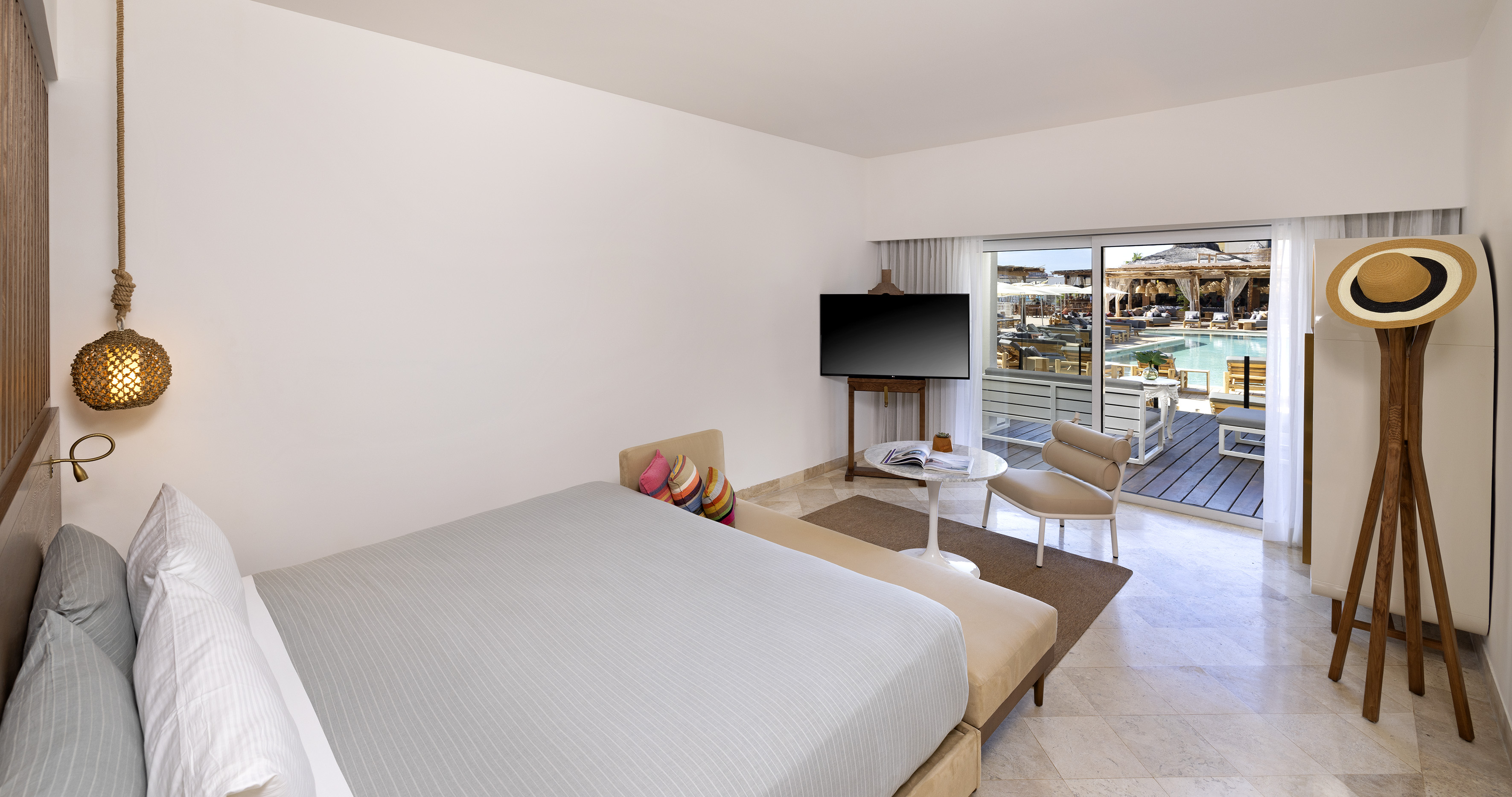 Modern hotel suite with pool view balcony, bed, and sitting area.
