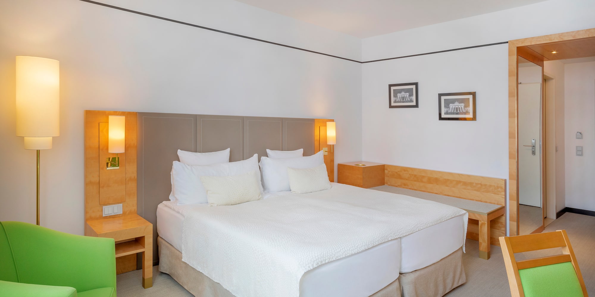 Modern hotel room with bright double bed, green accent chair, and wood furniture.