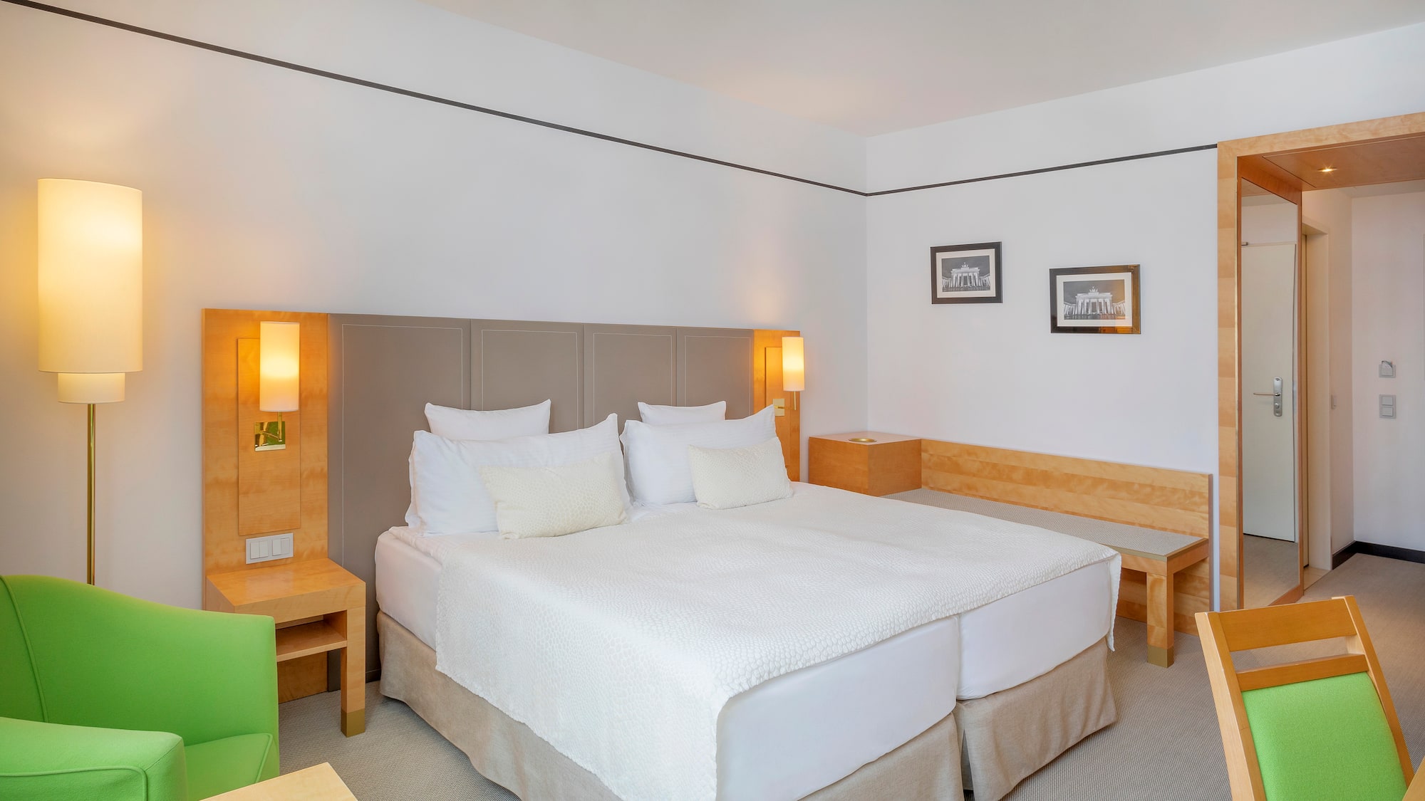 Modern hotel room with bright double bed, green accent chair, and wood furniture.