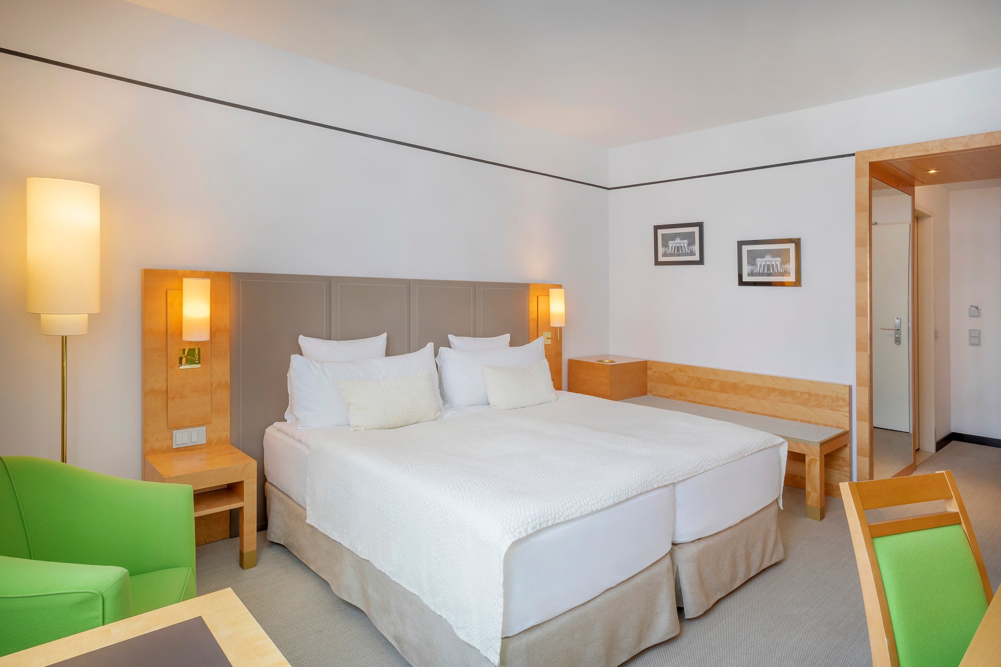 Modern hotel room with bright double bed, green accent chair, and wood furniture.