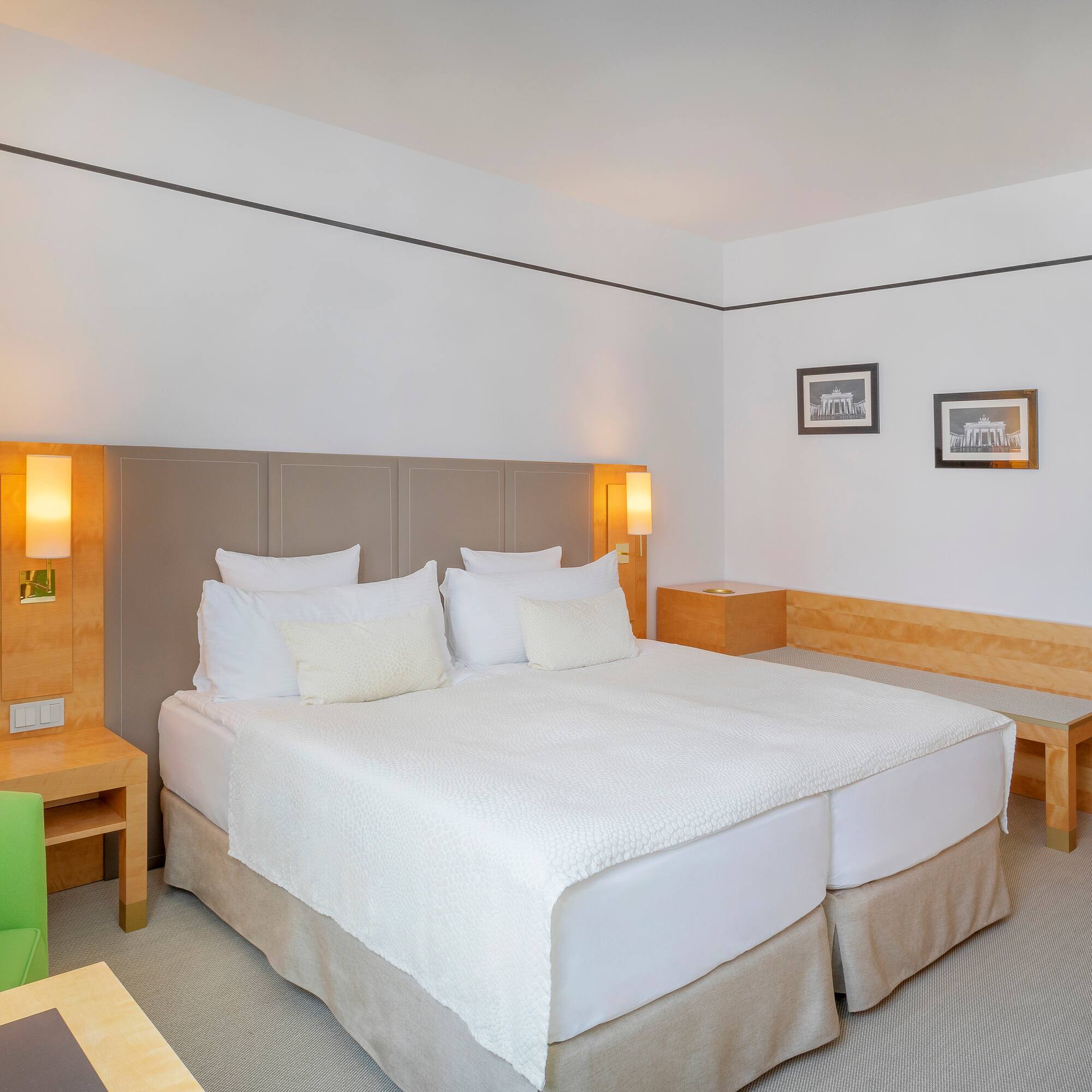 Modern hotel room with bright double bed, green accent chair, and wood furniture.
