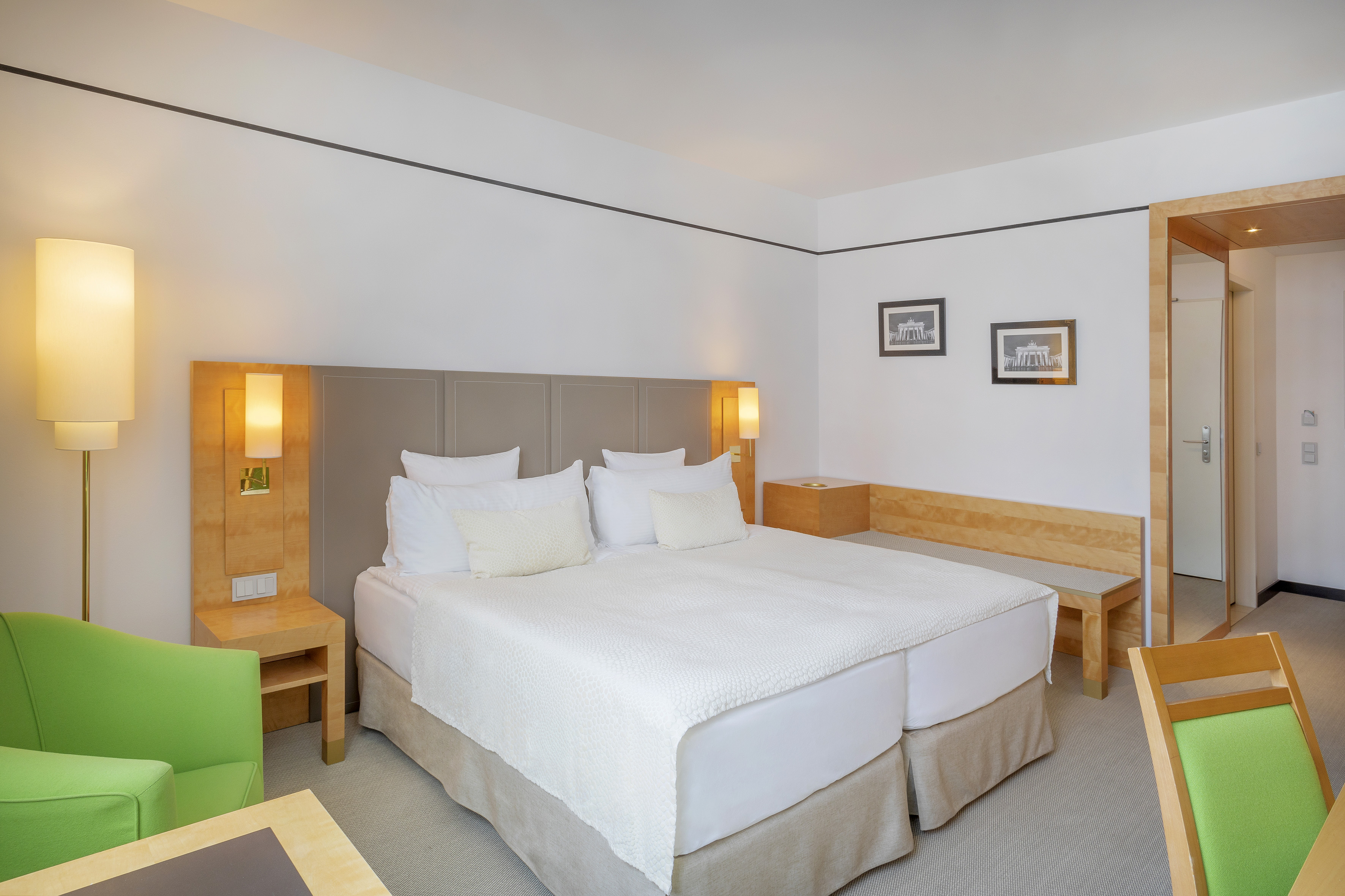 Modern hotel room with bright double bed, green accent chair, and wood furniture.