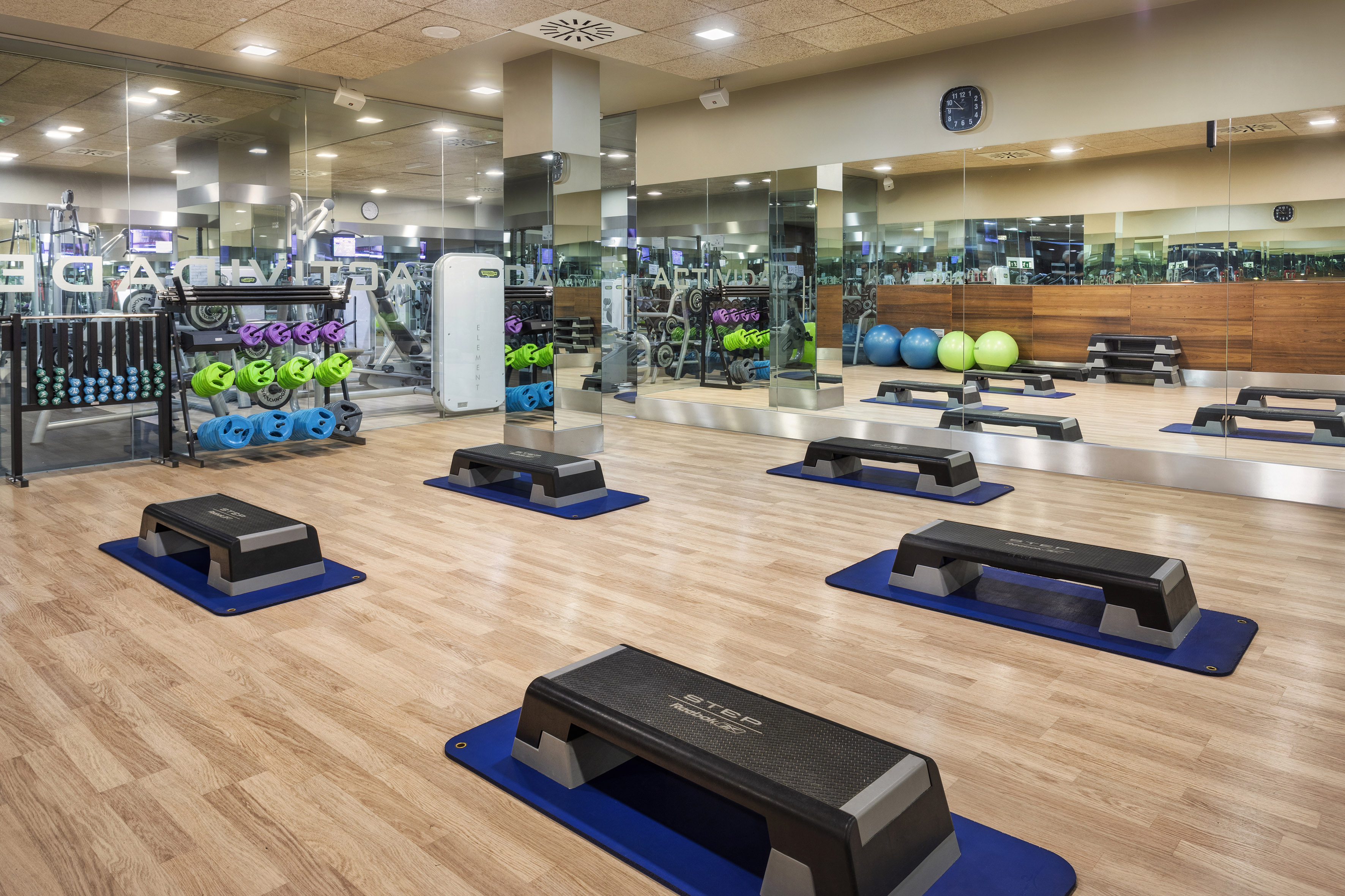 Fitness studio with step platforms, weight racks, exercise balls, and mirrored walls.