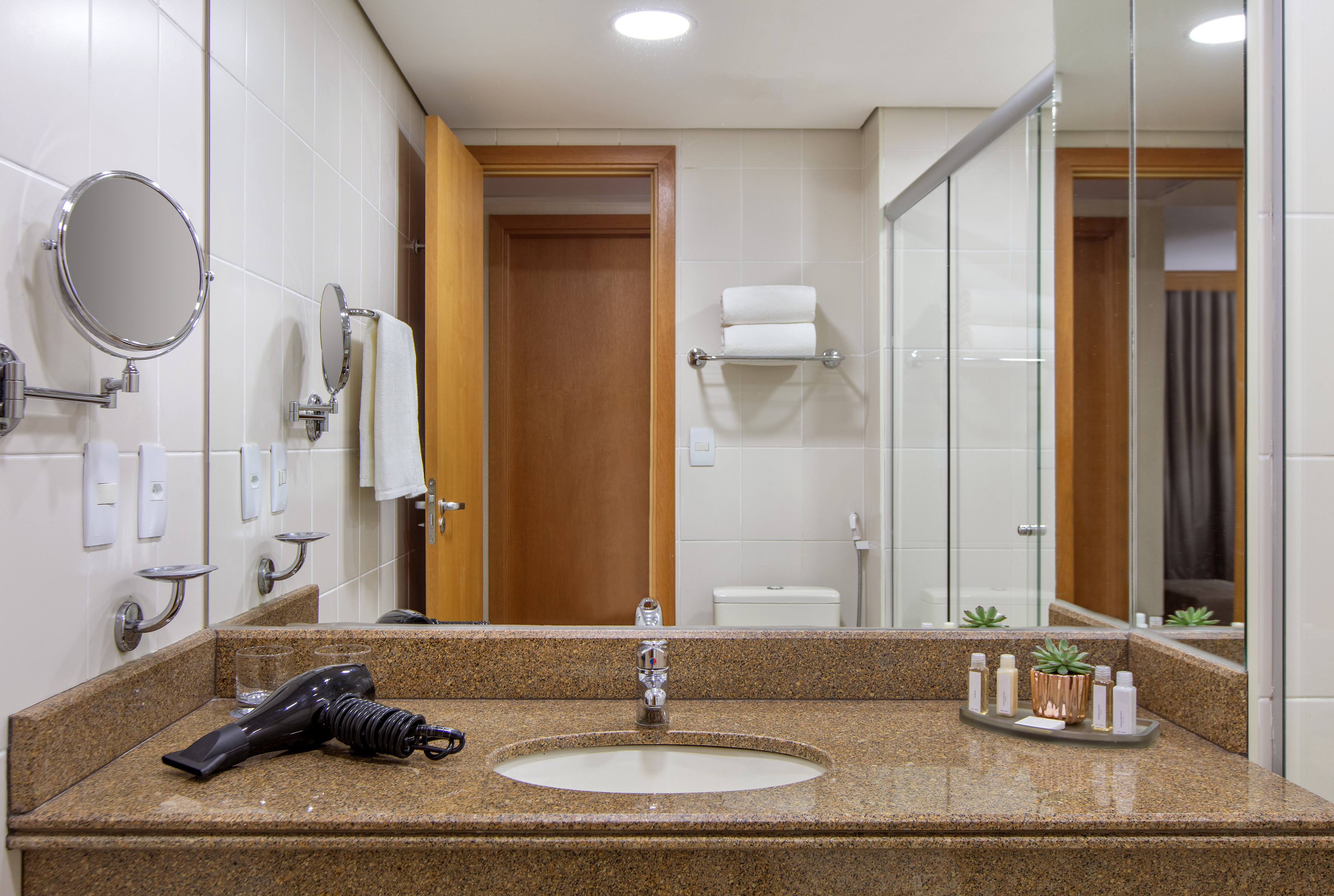 Modern hotel bathroom with granite vanity, mirror, hairdryer, and toiletries.