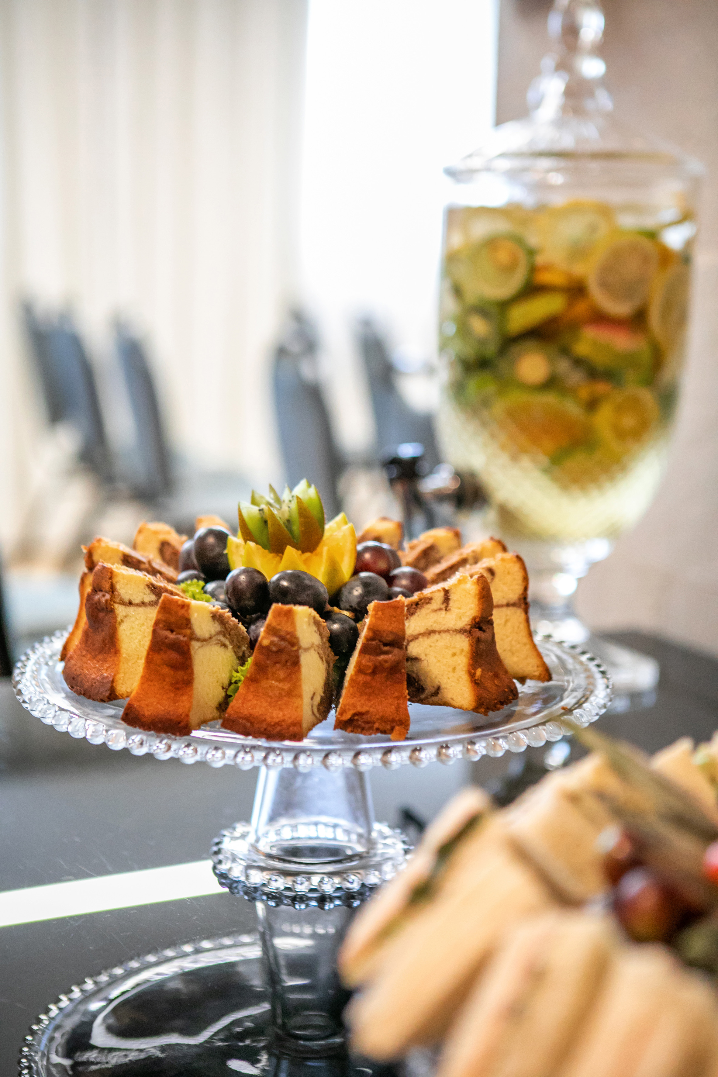 Marble cake slices with grapes, kiwi, orange on glass stand, fruit-infused water.