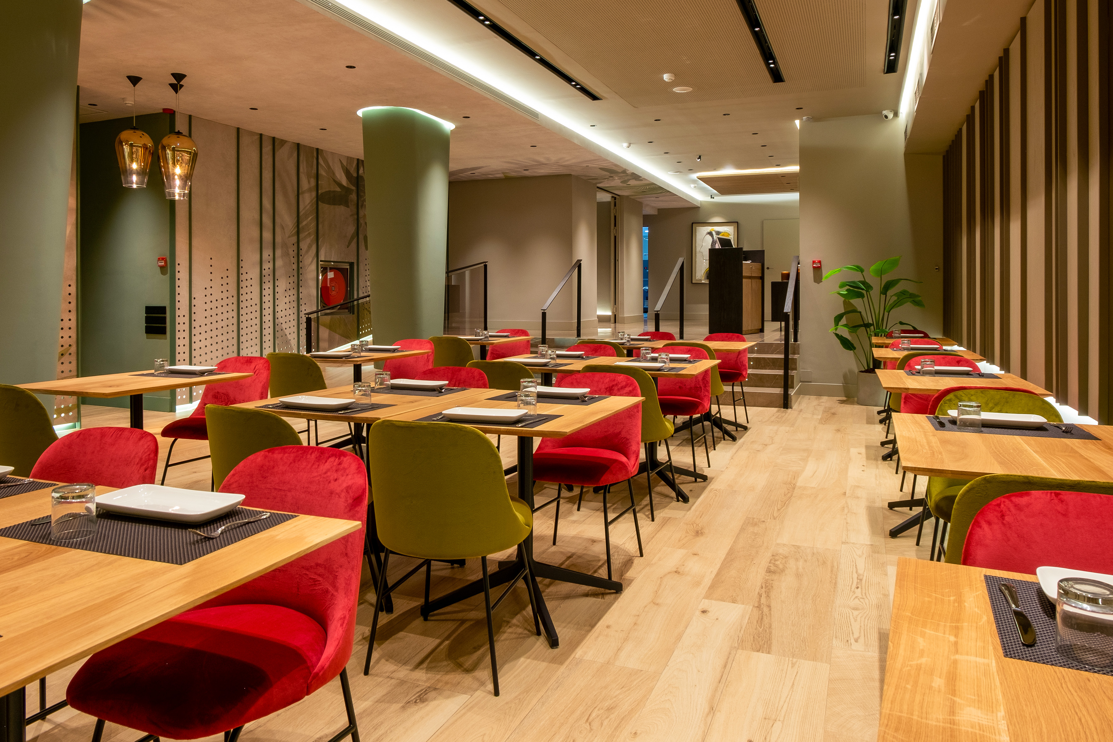 Modern restaurant dining room with wooden tables, red and green chairs.