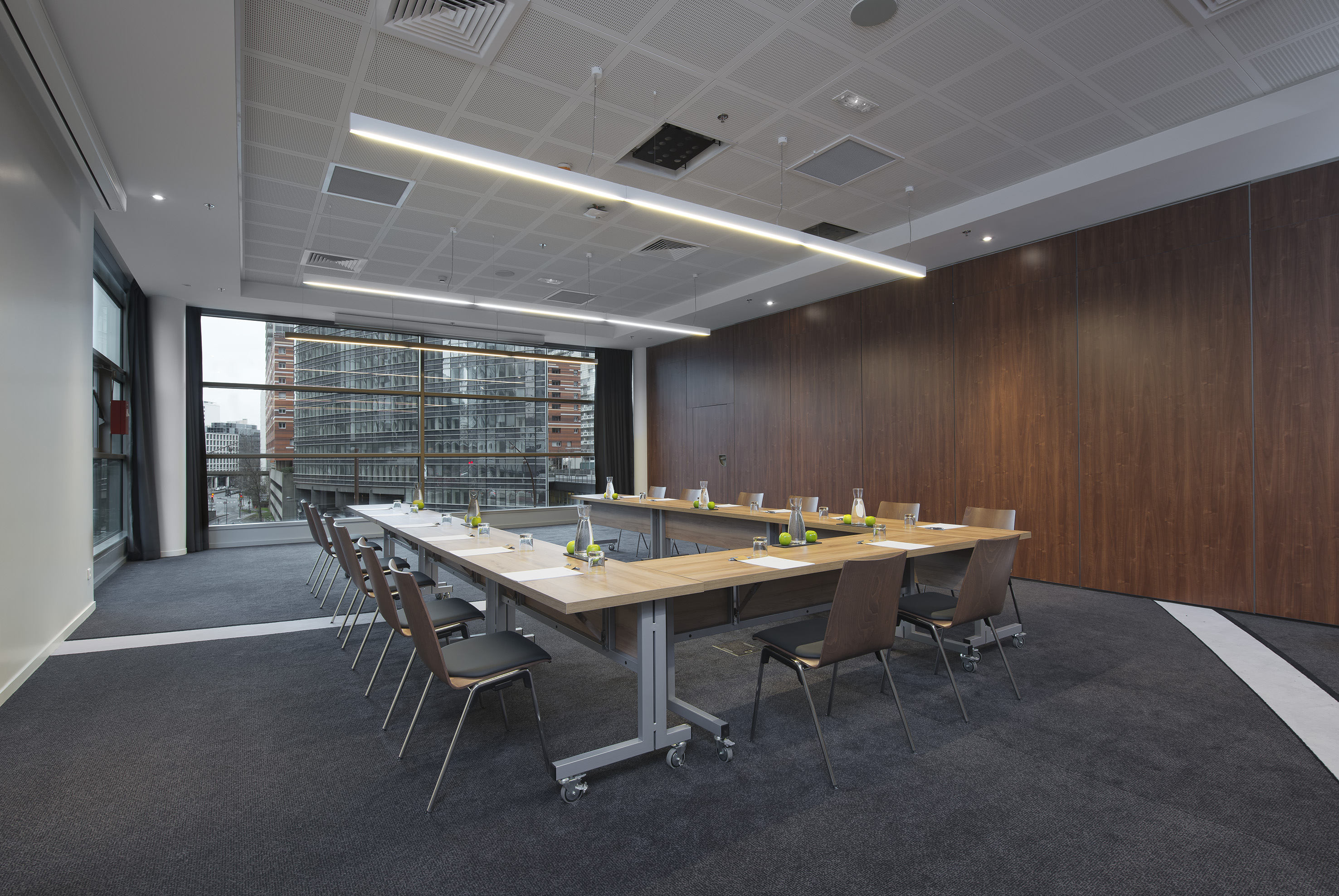 Modern U-shaped conference room with city view, large window, and wooden wall.