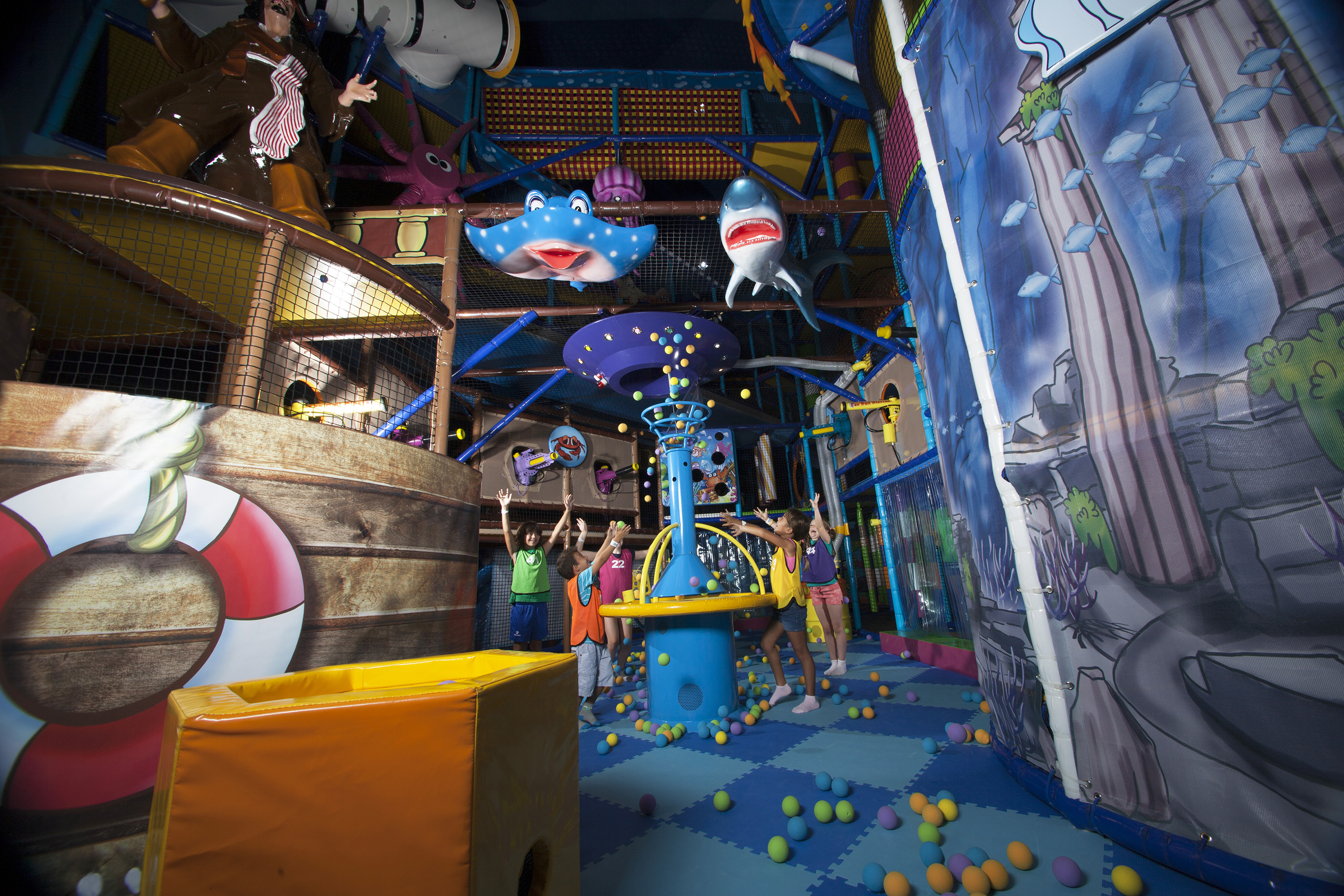 Children playing in a colorful indoor playground with a ball pit and pirate theme.