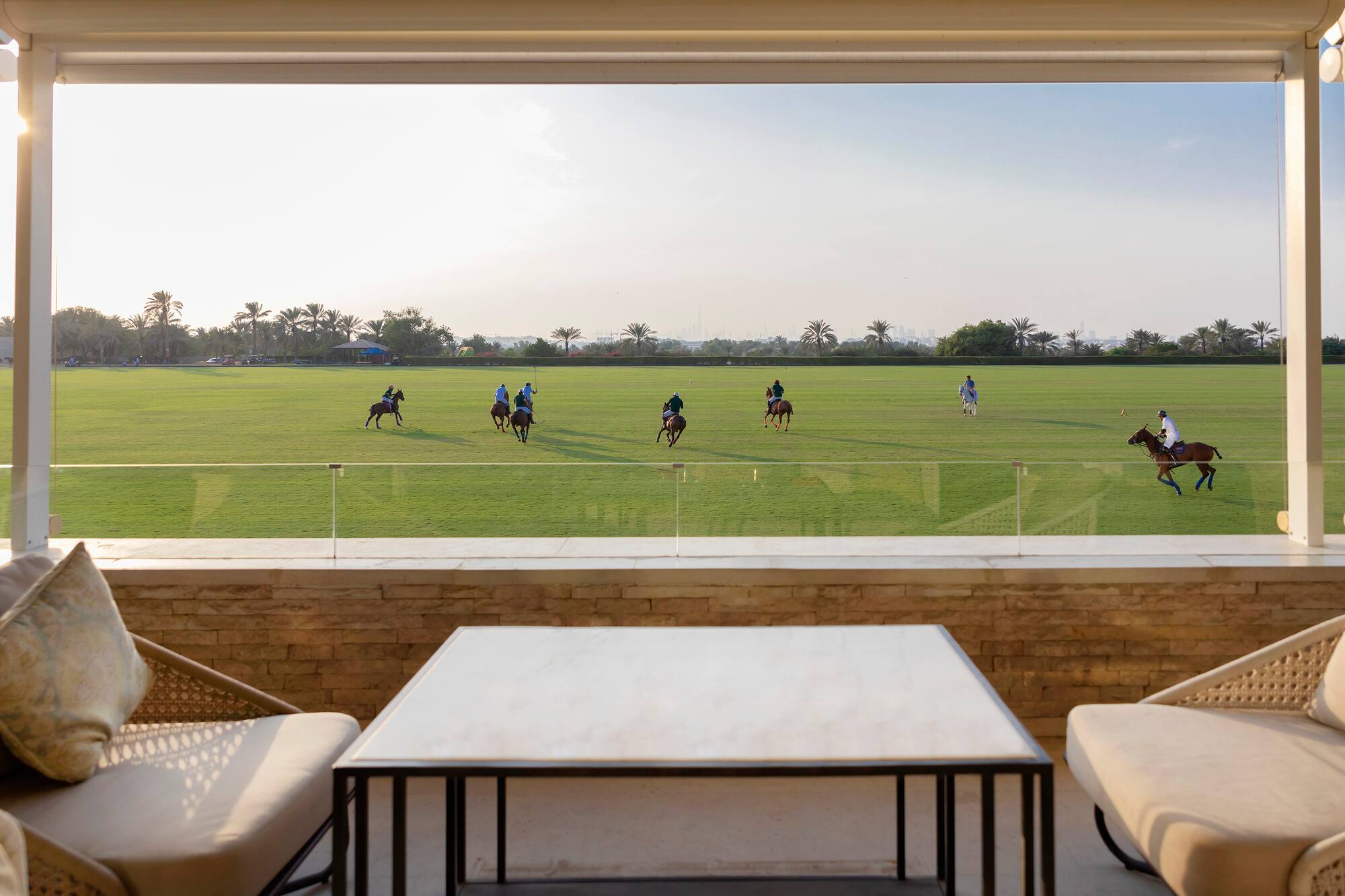 Polo match on green field from luxury terrace, players on horseback.