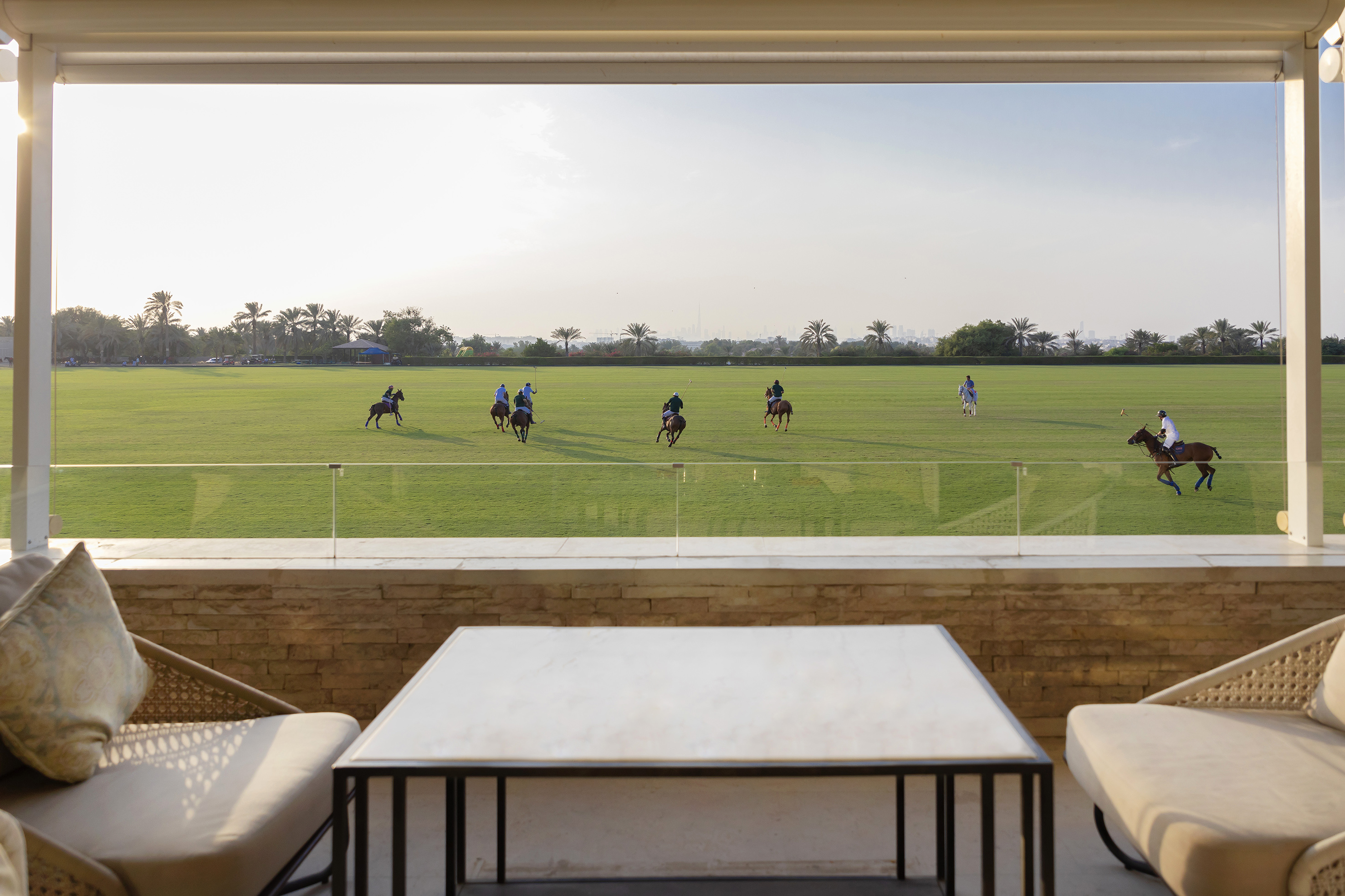 Polo match on green field from luxury terrace, players on horseback.