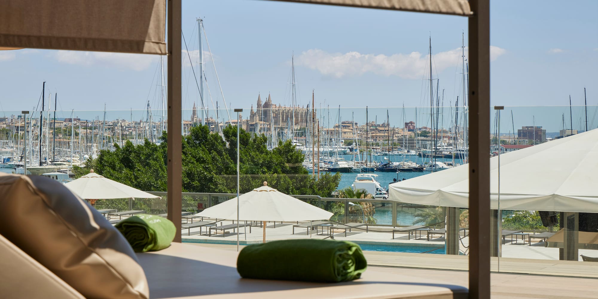 Luxury daybed overlooking Palma marina with cathedral, sailboats, and pool.