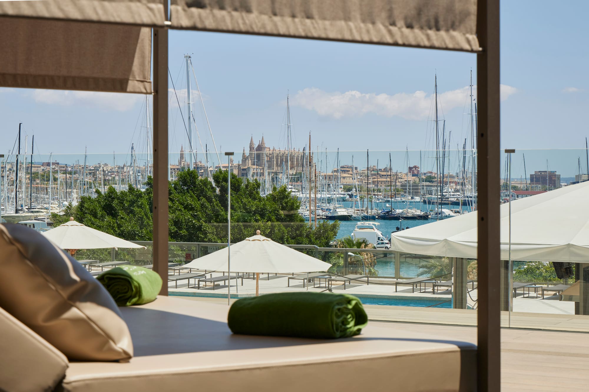 Luxury daybed overlooking Palma marina with cathedral, sailboats, and pool.