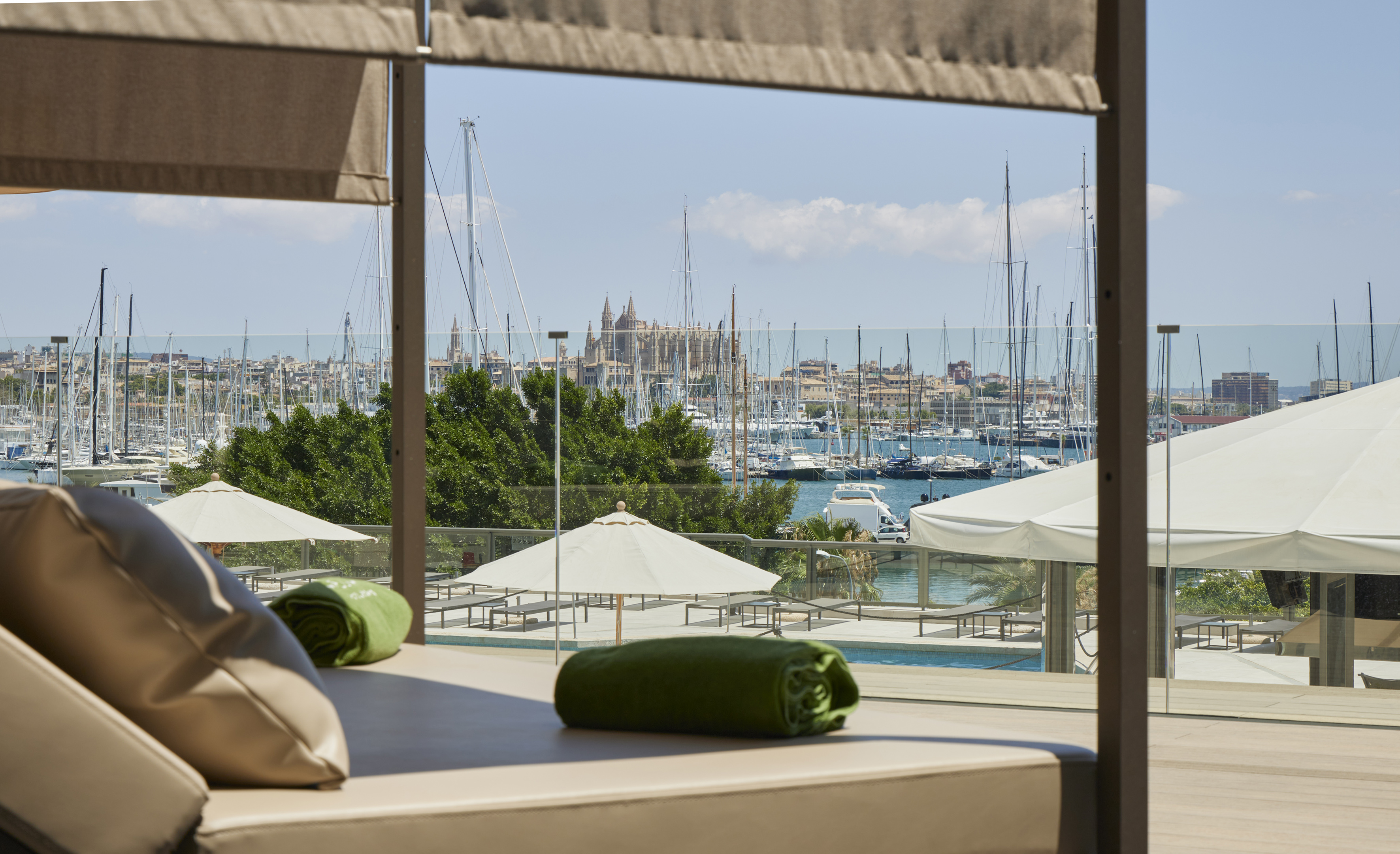 Luxury daybed overlooking Palma marina with cathedral, sailboats, and pool.