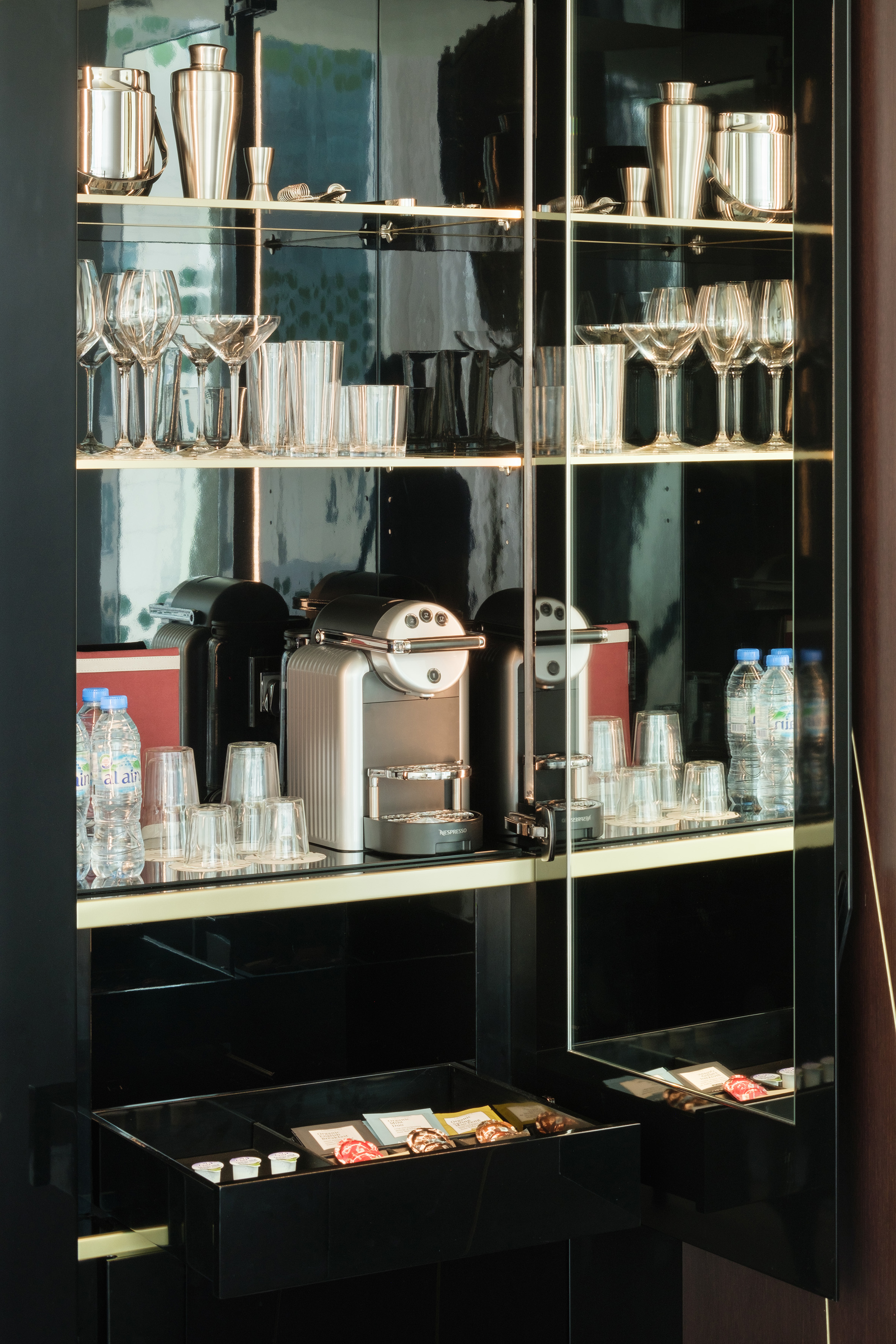 Luxury hotel minibar with Nespresso machine, bar tools, glassware, and snacks.