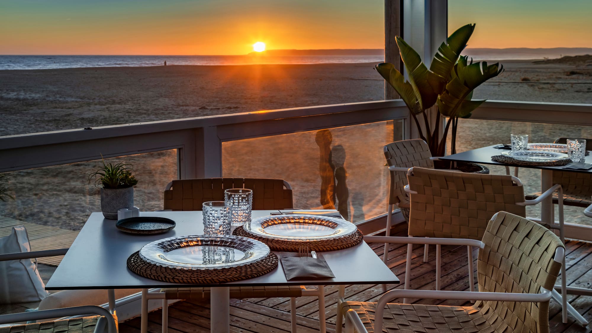 a table with plates and glasses on it with a sunset in the background