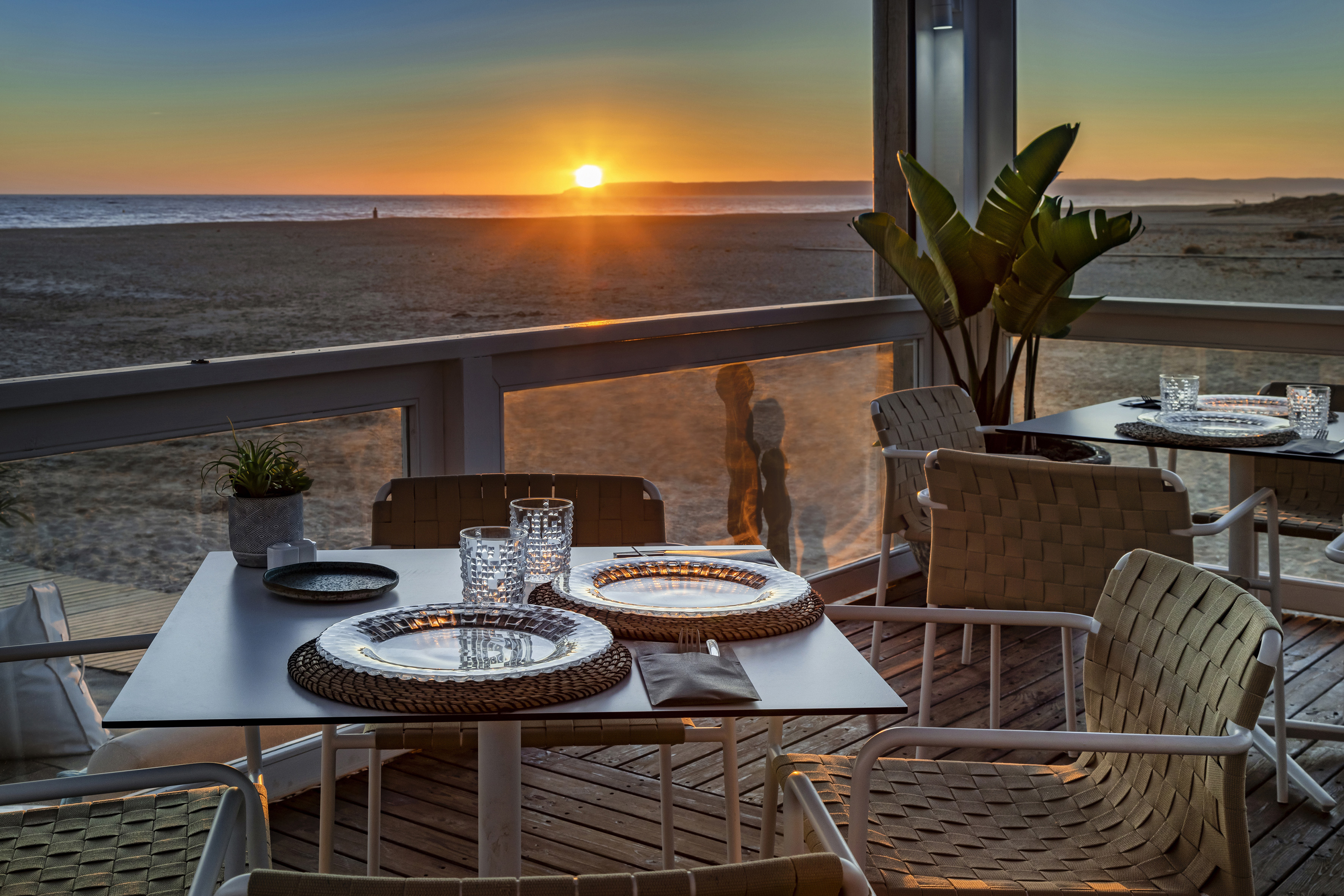 Beach restaurant sunset dining with ocean view, set tables.