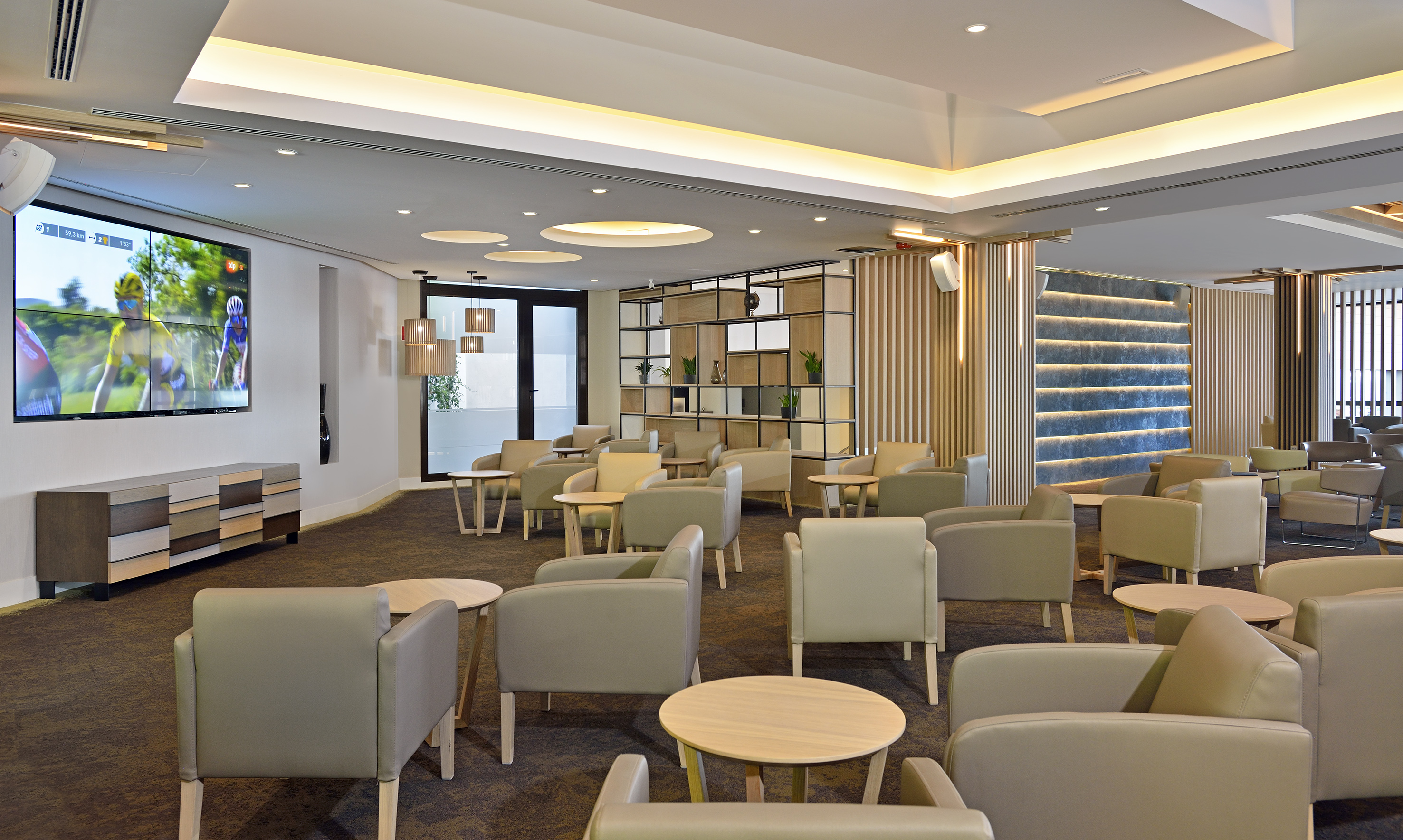 Stylish hotel lounge with contemporary seating, tables, and large TV display.