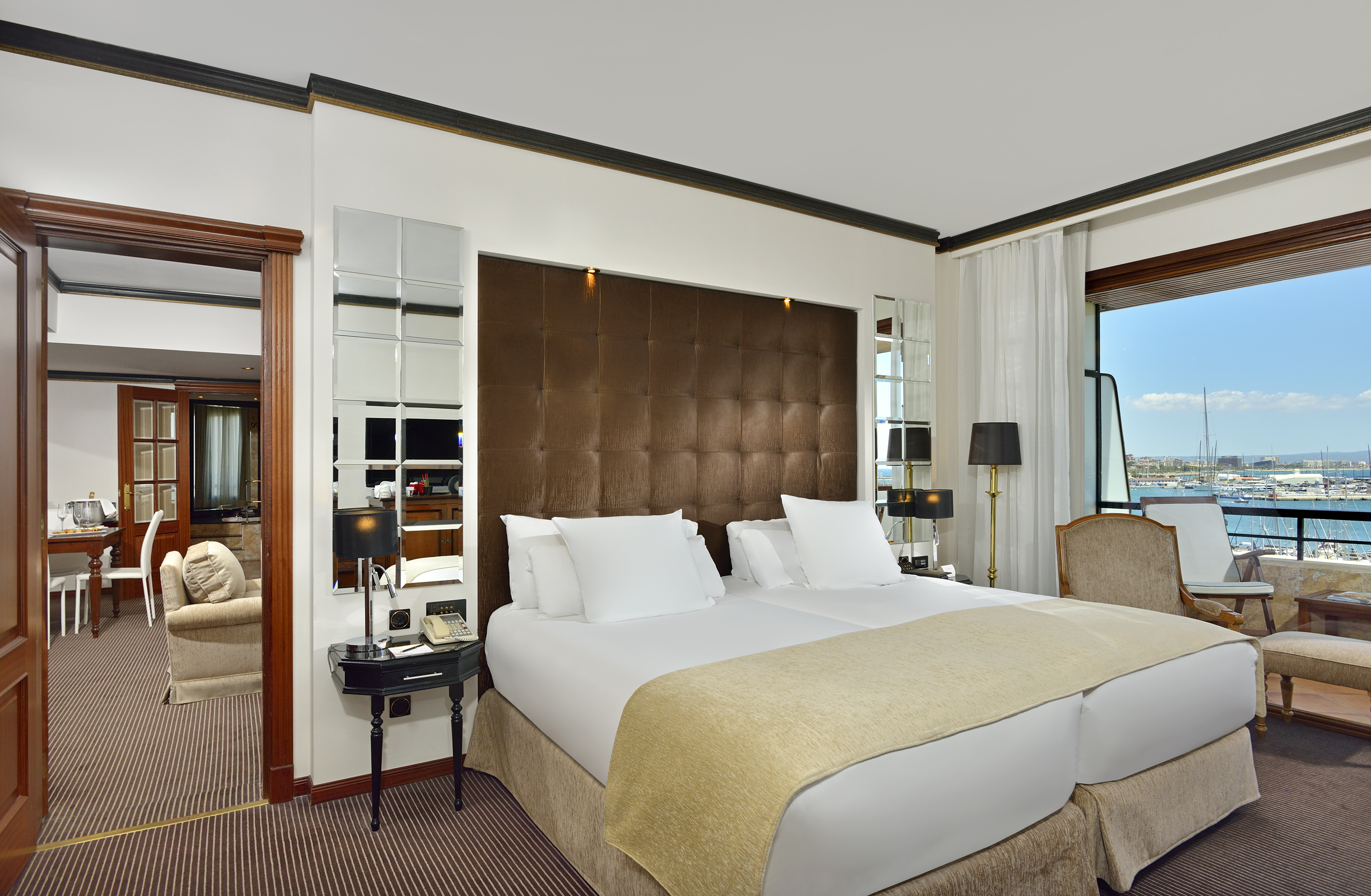 Luxury hotel bedroom with twin beds, upholstered headboard, and marina view.