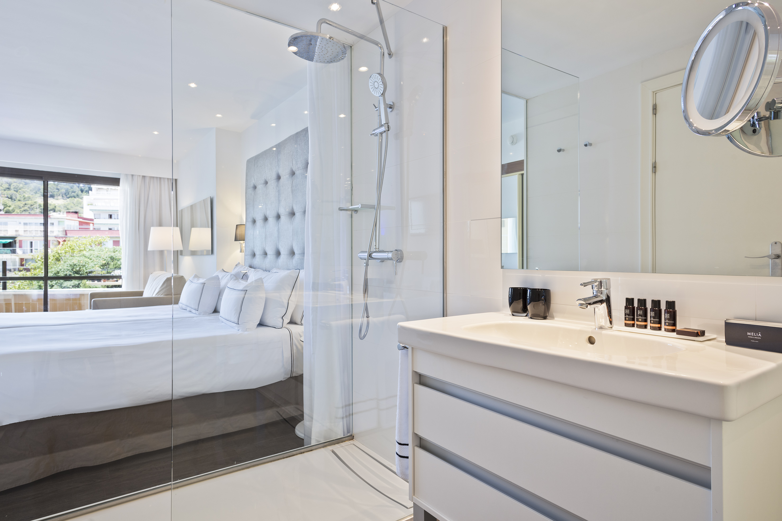Bright, modern hotel room with glass shower, vanity, and comfortable bed.