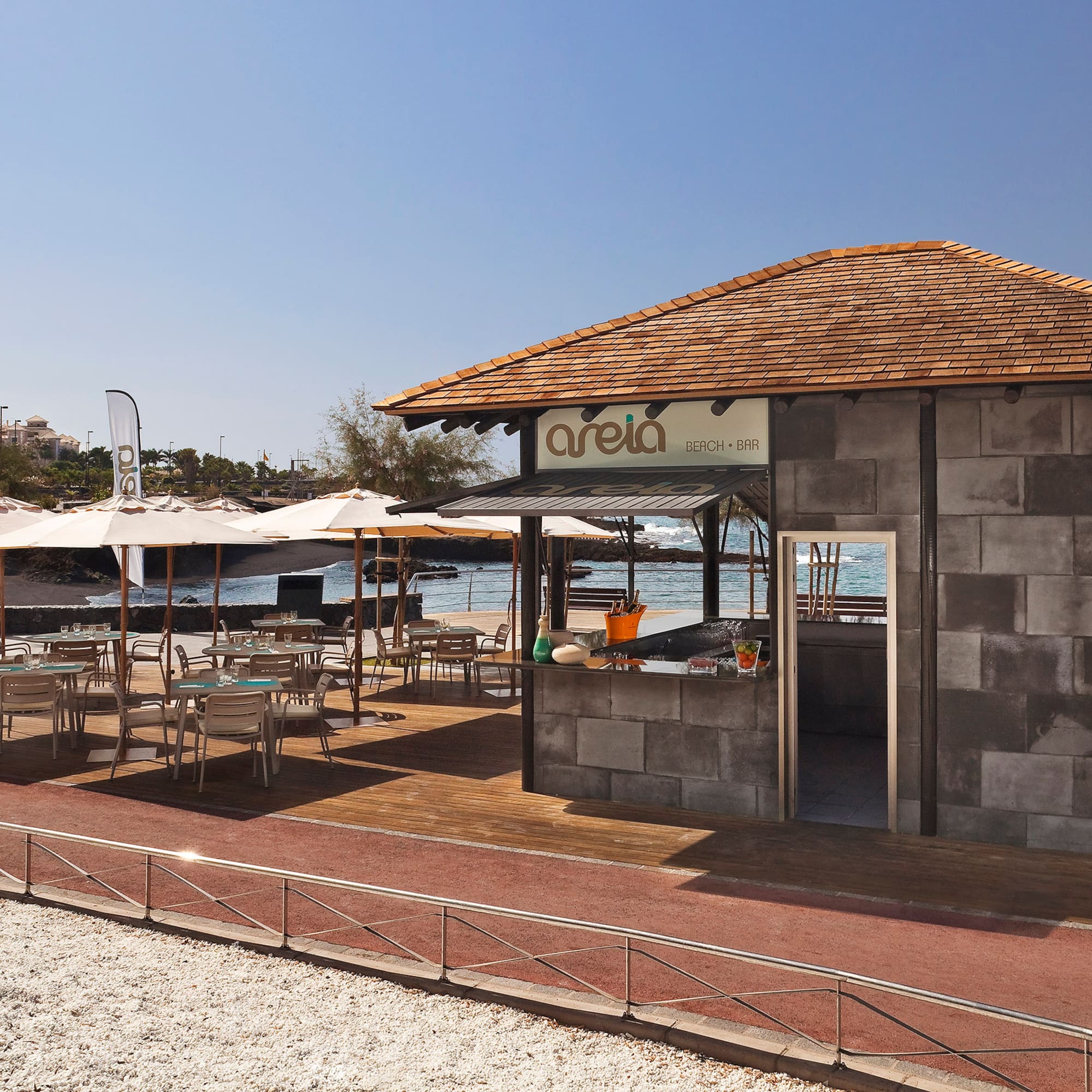 Areia Beach Bar: outdoor dining on wooden deck with umbrellas, ocean view.