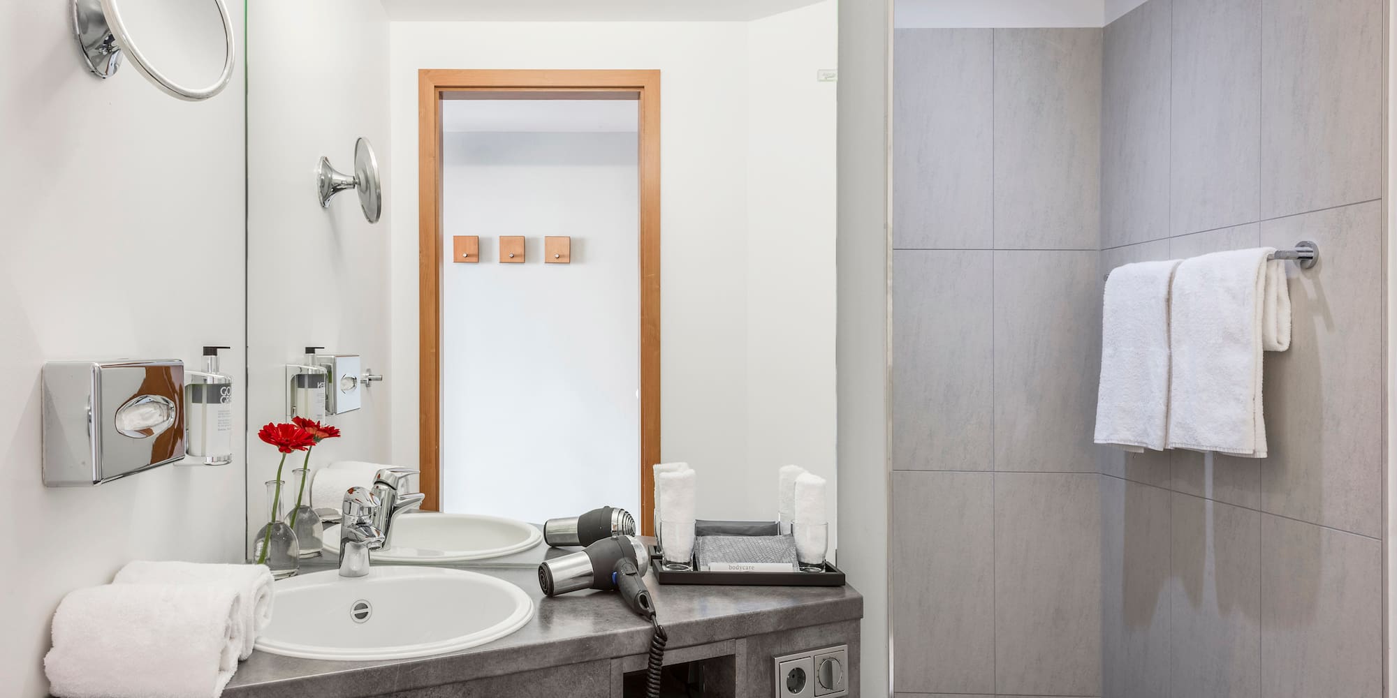 Modern hotel bathroom featuring a vanity, sink, hairdryer, and tiled shower.