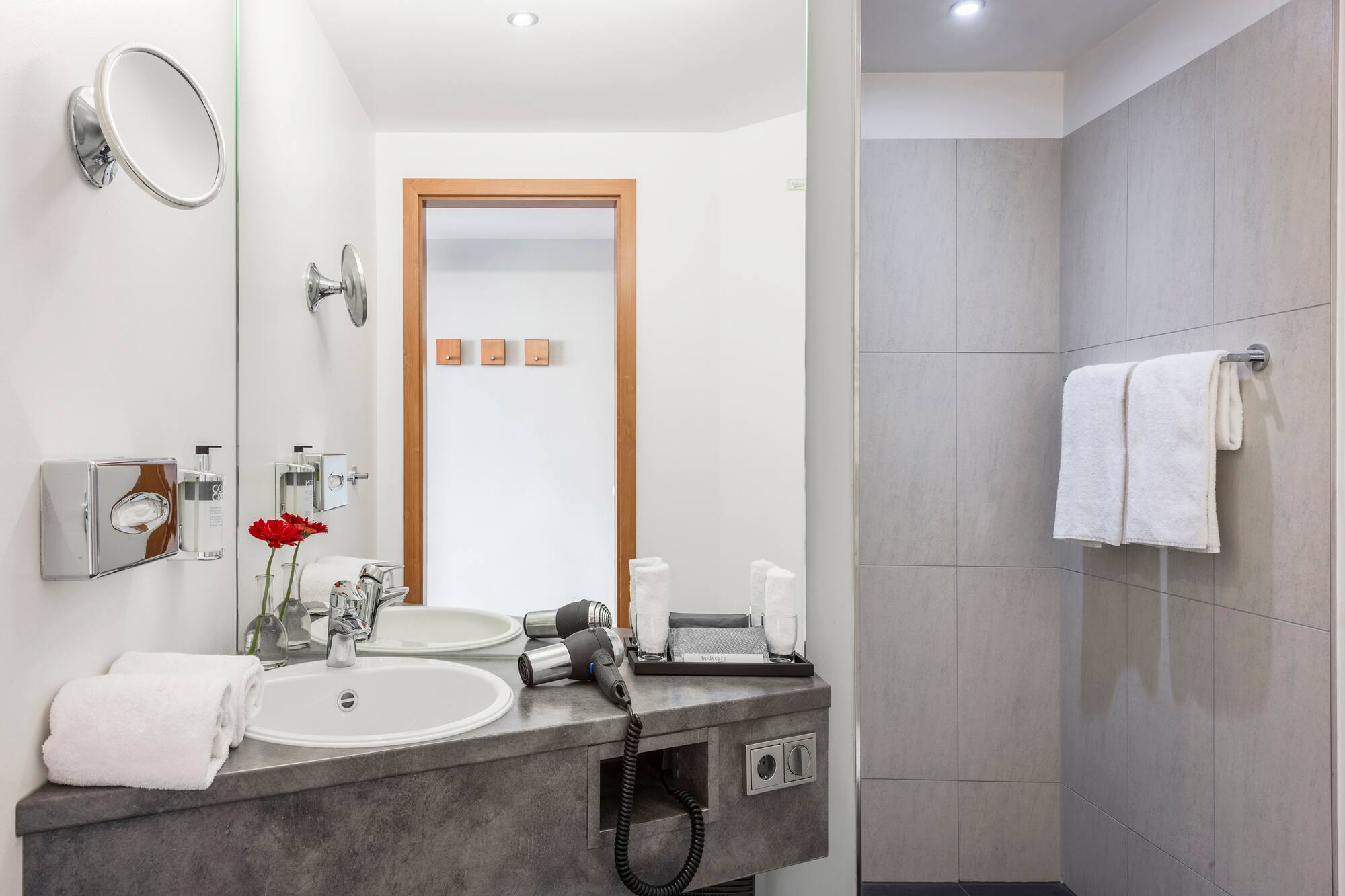 Modern hotel bathroom with sink, mirror, hairdryer, shower, and fresh towels.