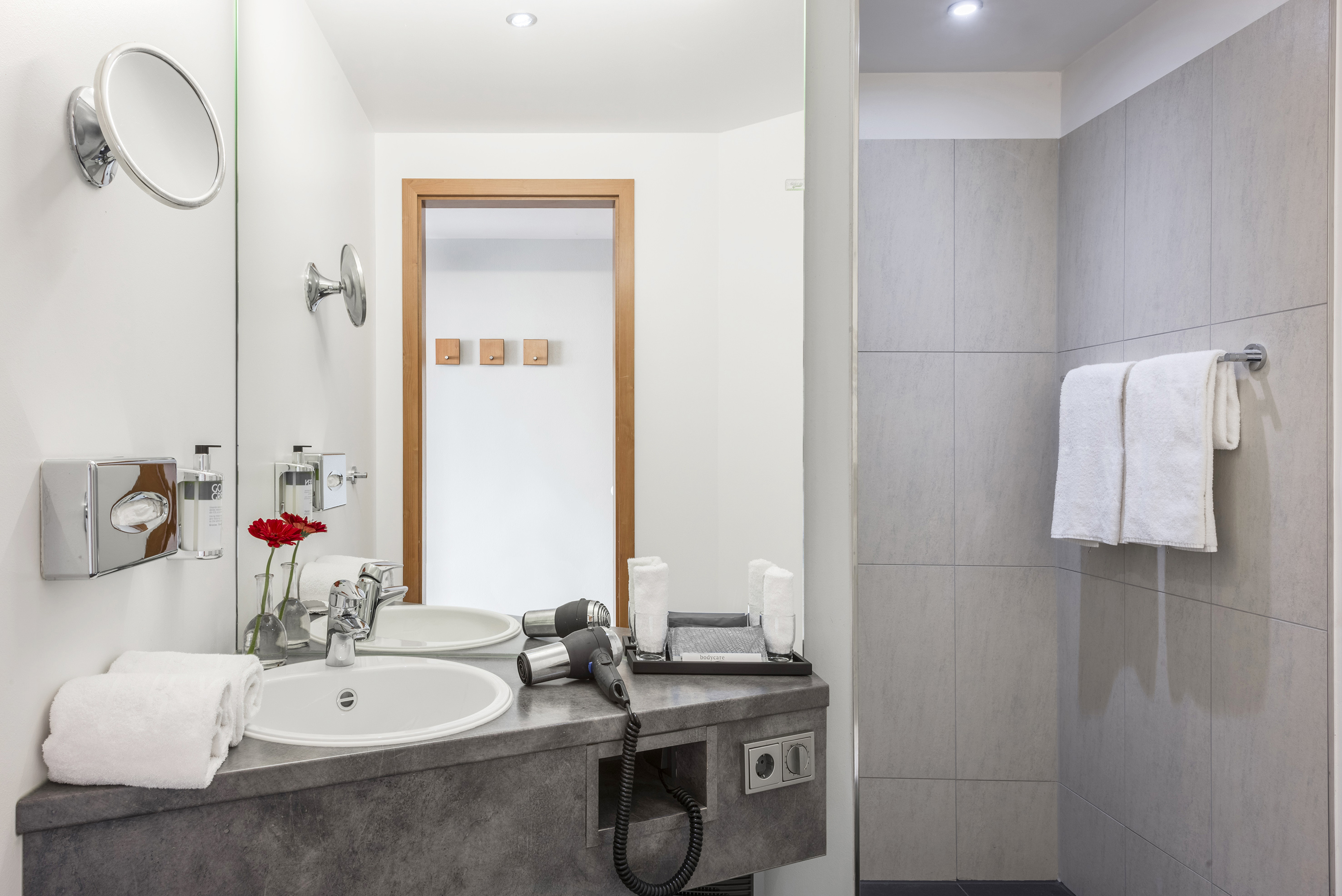 Modern hotel bathroom featuring a vanity, sink, hairdryer, and tiled shower.