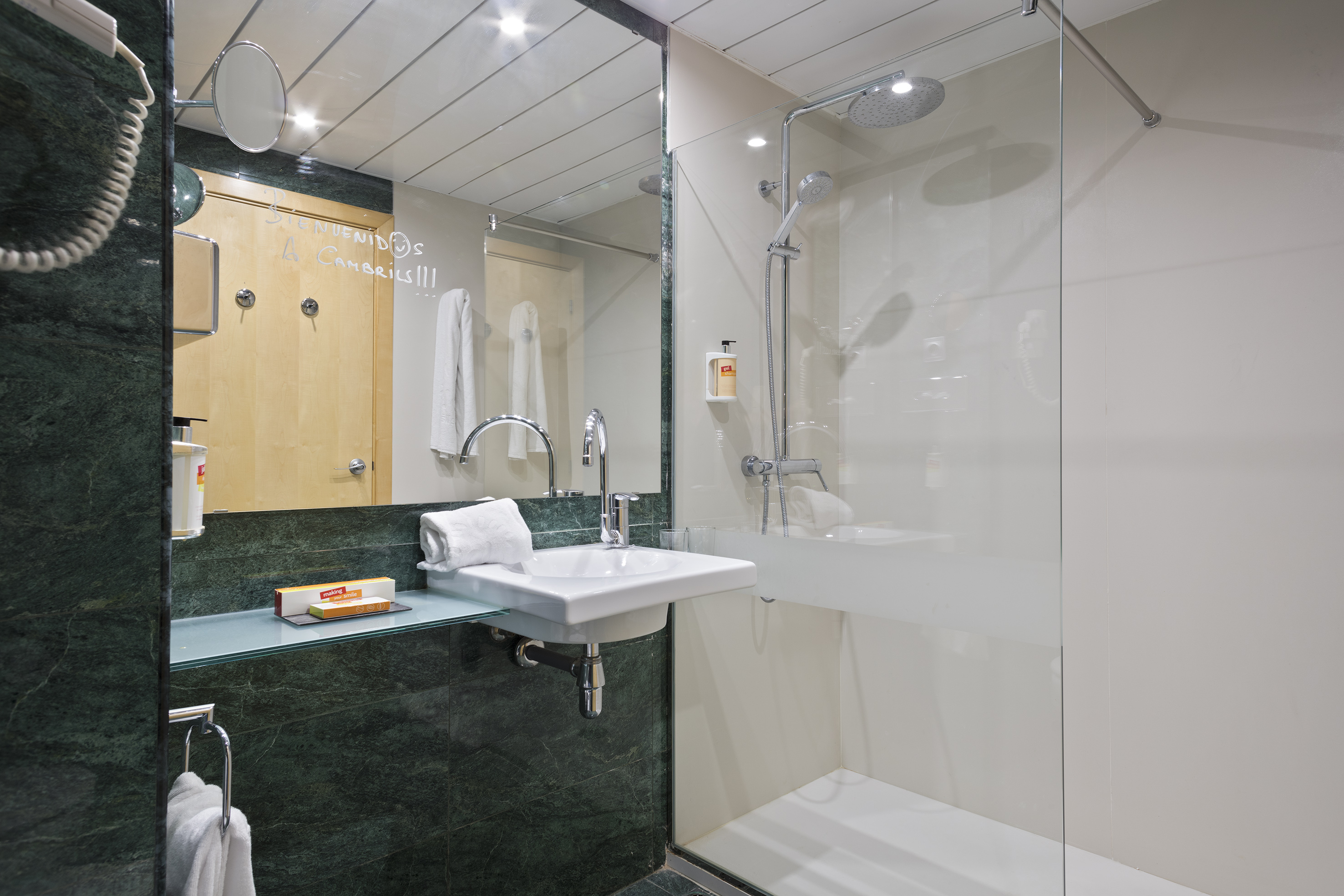 Cambrils hotel bathroom: green marble, modern sink, and glass walk-in shower.