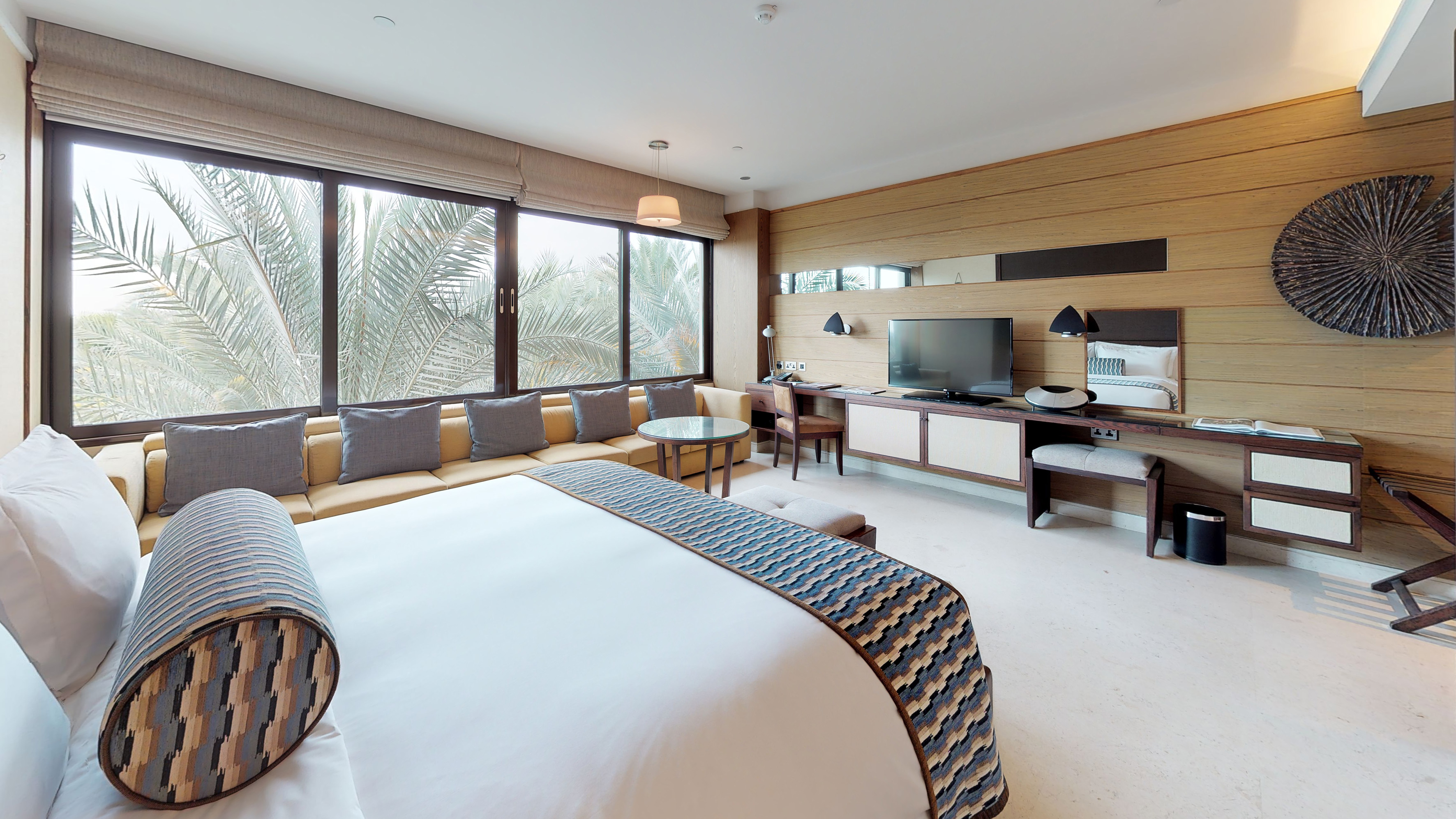 Modern hotel room with palm tree view, king bed, sofa lounge, and wooden interior.