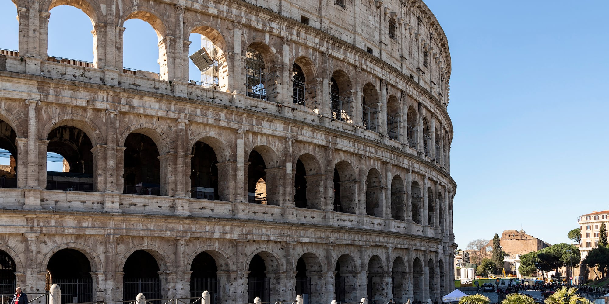a large stone building with many arches with Colosseum in the background