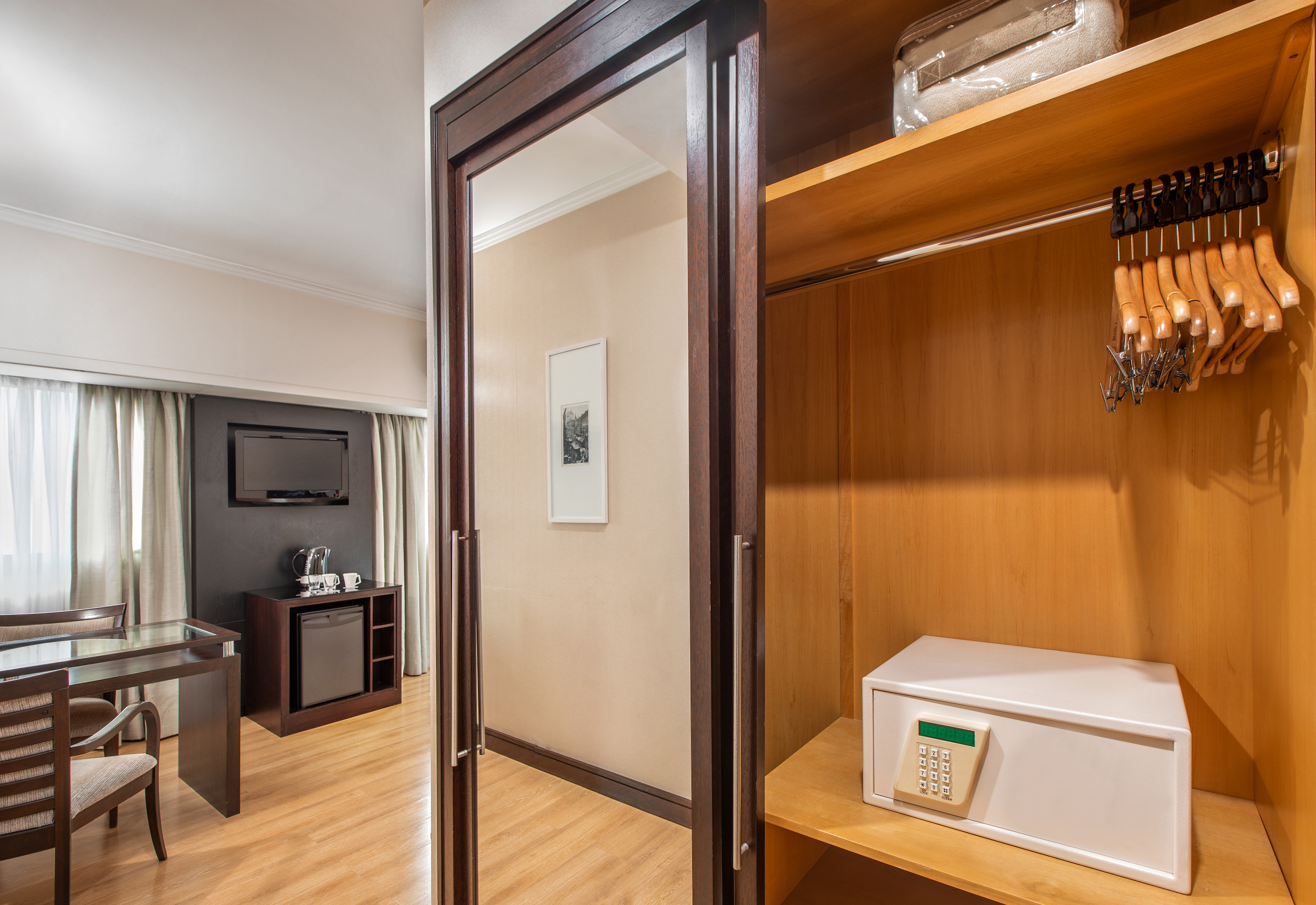 Hotel room wardrobe with safe, hangers, reflecting desk and TV area.