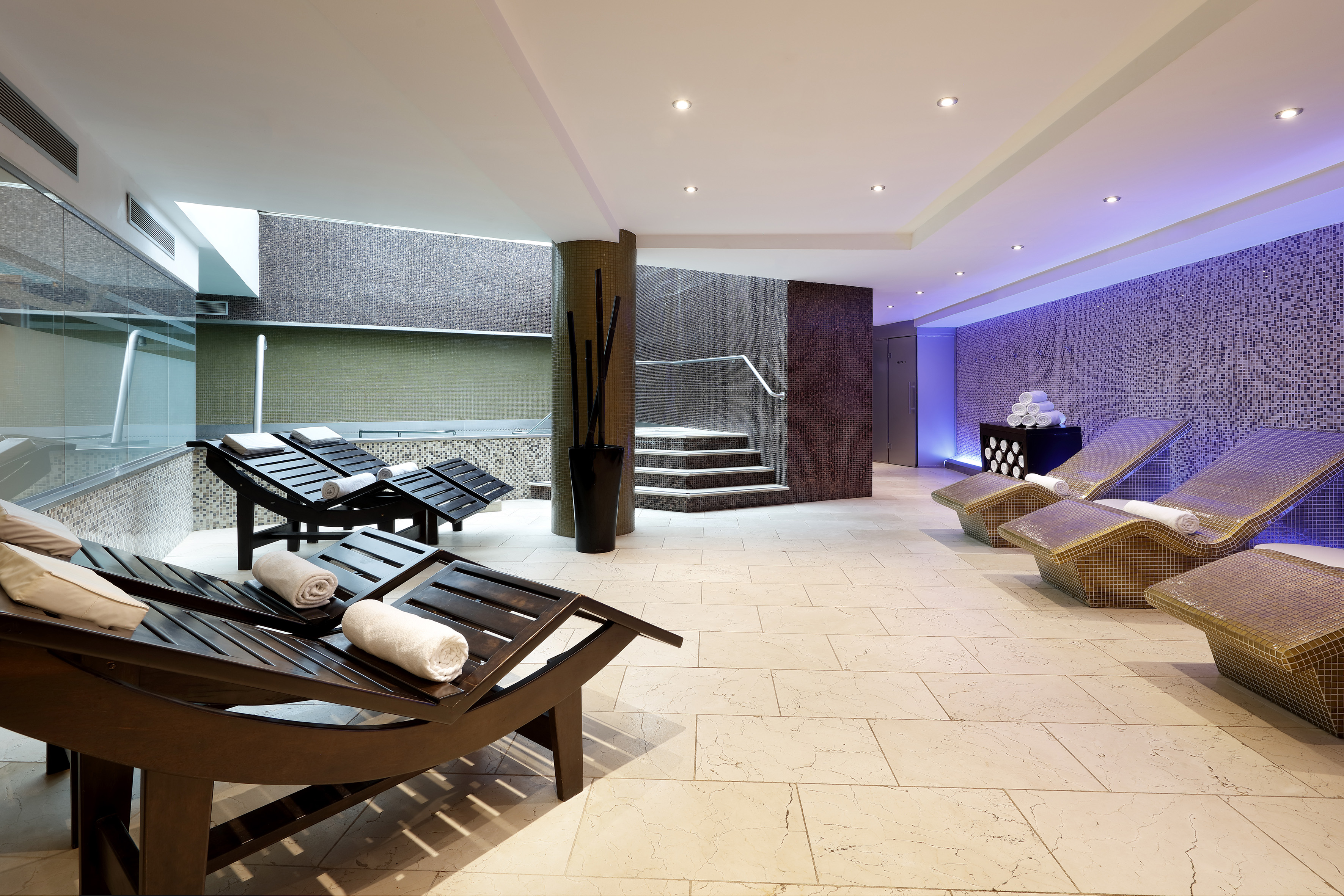 Modern spa relaxation area with lounge chairs, mosaic walls, and indoor pool.