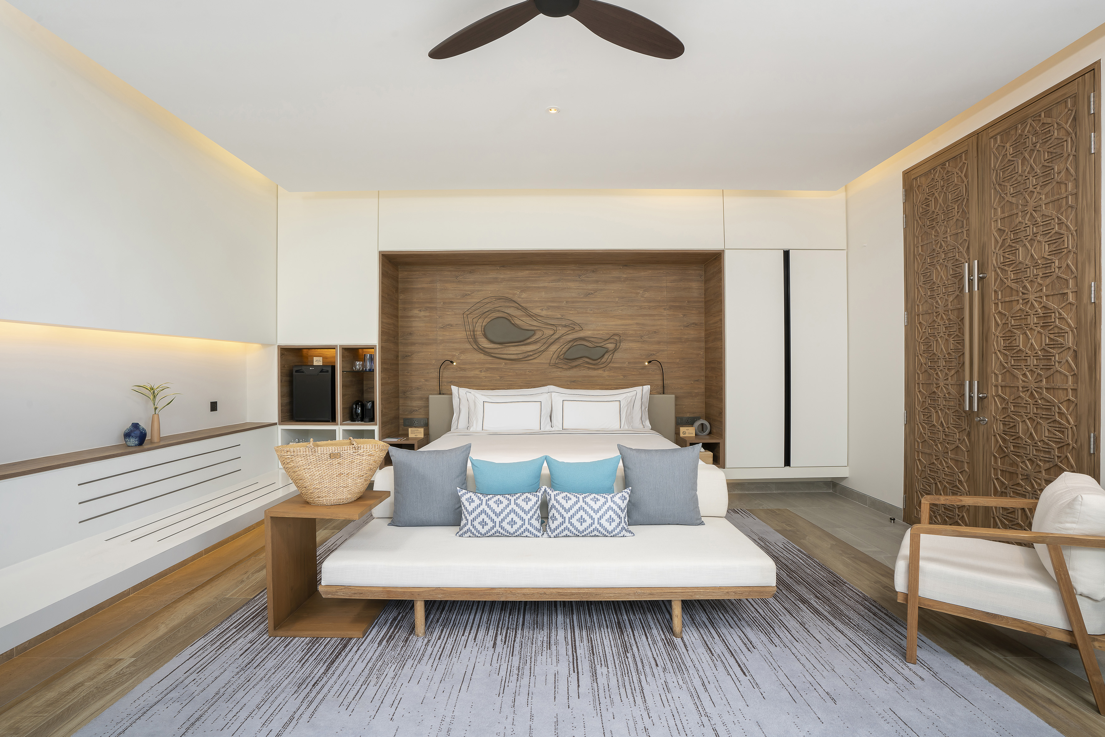 Modern bedroom suite with large bed, daybed, wood accents, and ornate carved doors.