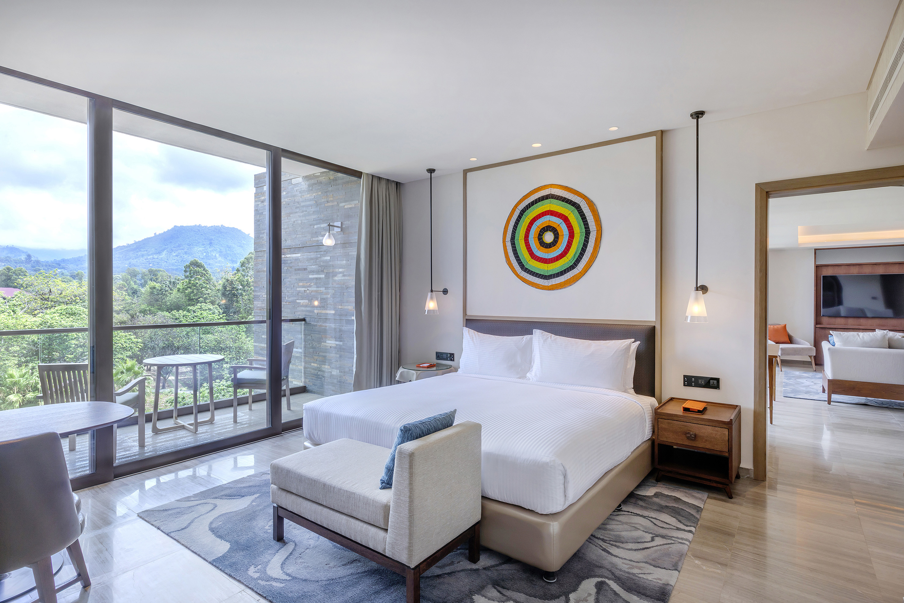 Modern hotel suite with mountain view balcony, king bed, colorful art.