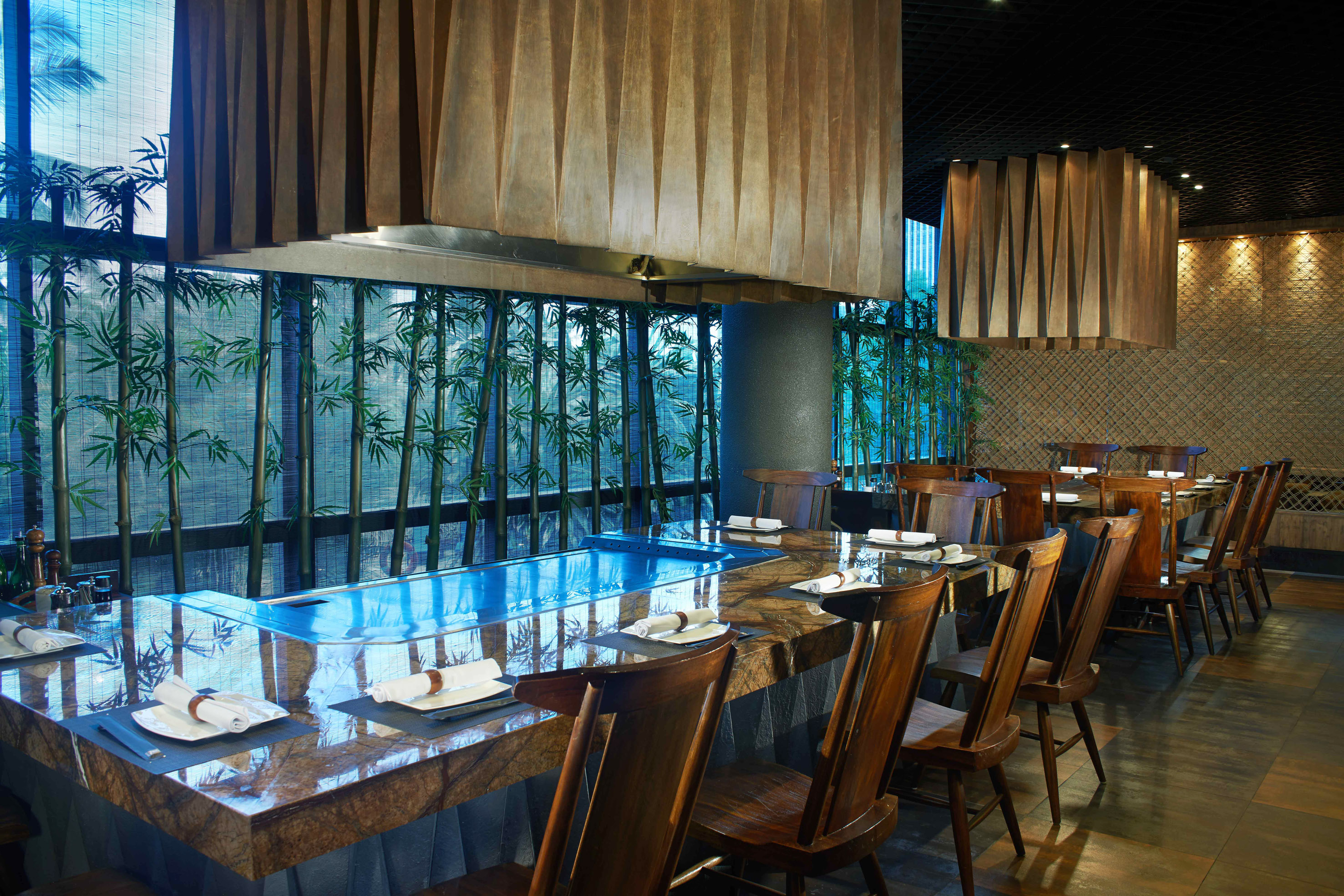 Teppanyaki restaurant with granite grill table, wooden chairs, and bamboo decor.