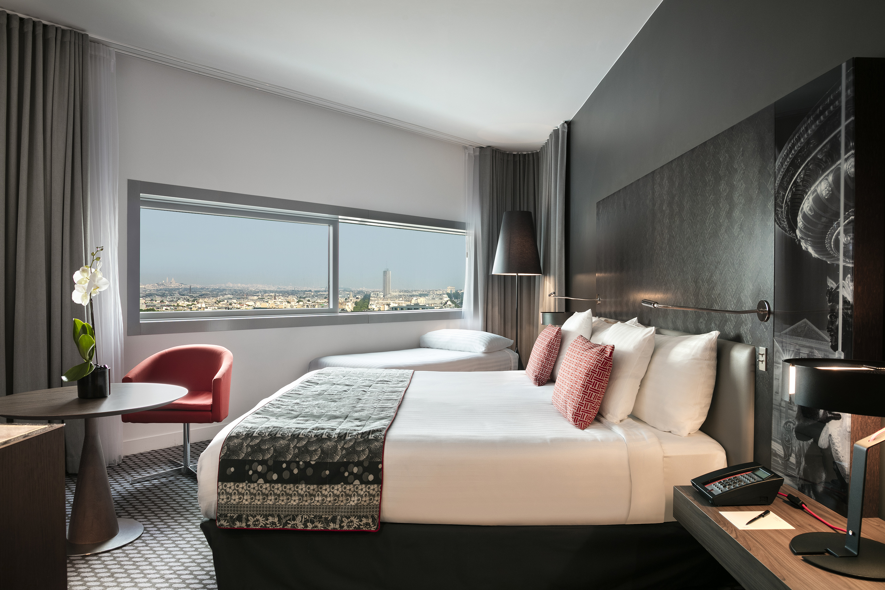 Elegant hotel room with Paris city view, king bed, daybed, and red chair.
