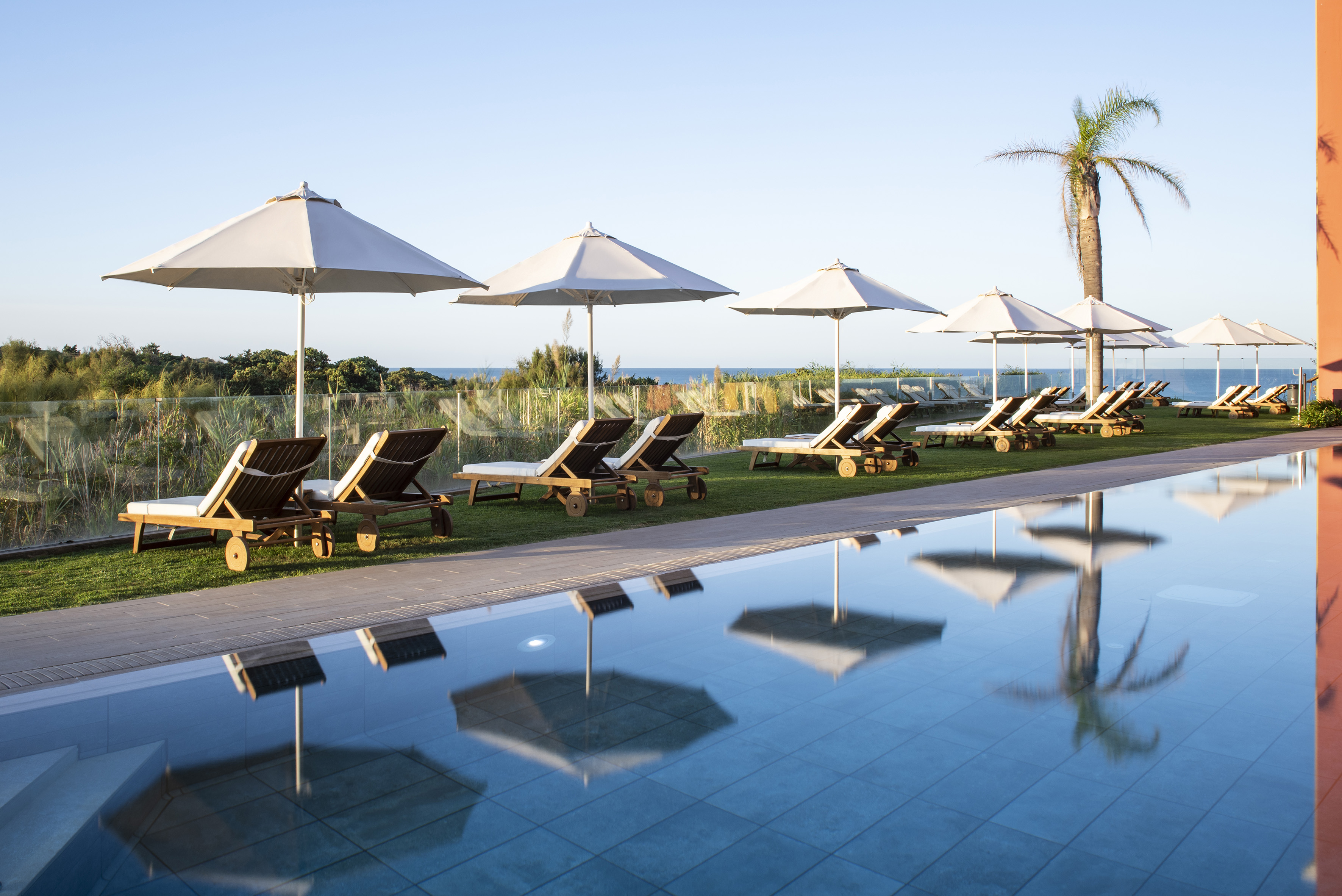 Poolside lounge chairs and umbrellas by the ocean at a resort.